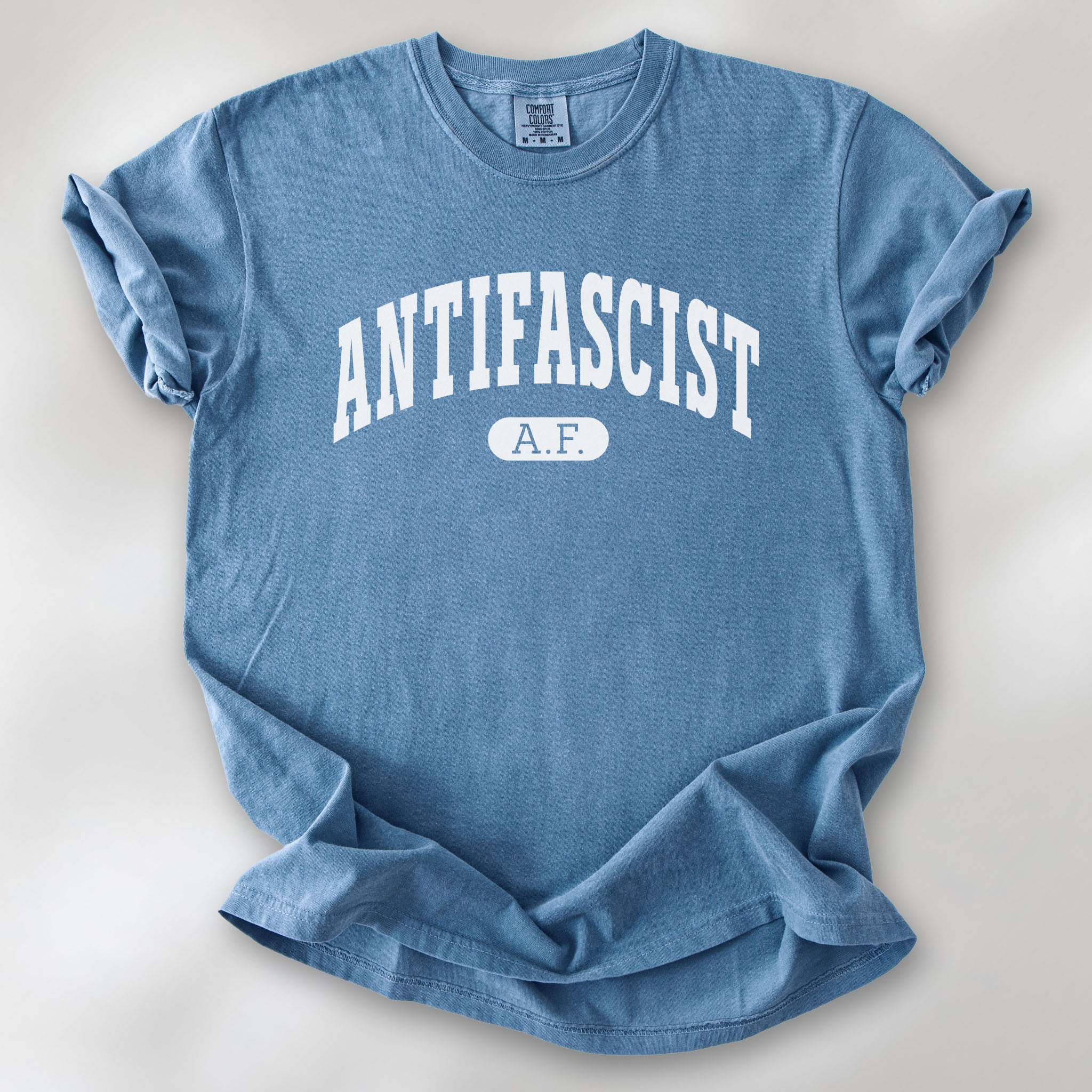 Blue jean Comfort Colors t-shirt with varsity collegiate style text across the front that reads "Antifascist AF."