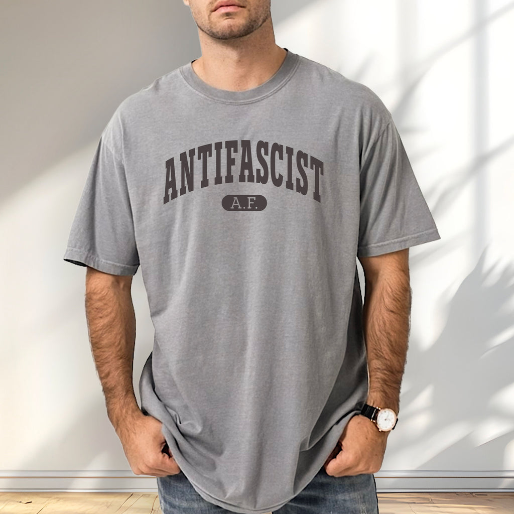 Male model wearing grey Comfort Colors t-shirt with varsity collegiate style text across the front that reads "Antifascist AF."