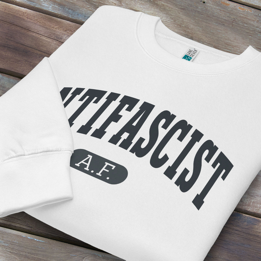 Folded white crewneck sweatshirt with varsity collegiate style text across the front that reads "Antifascist AF."