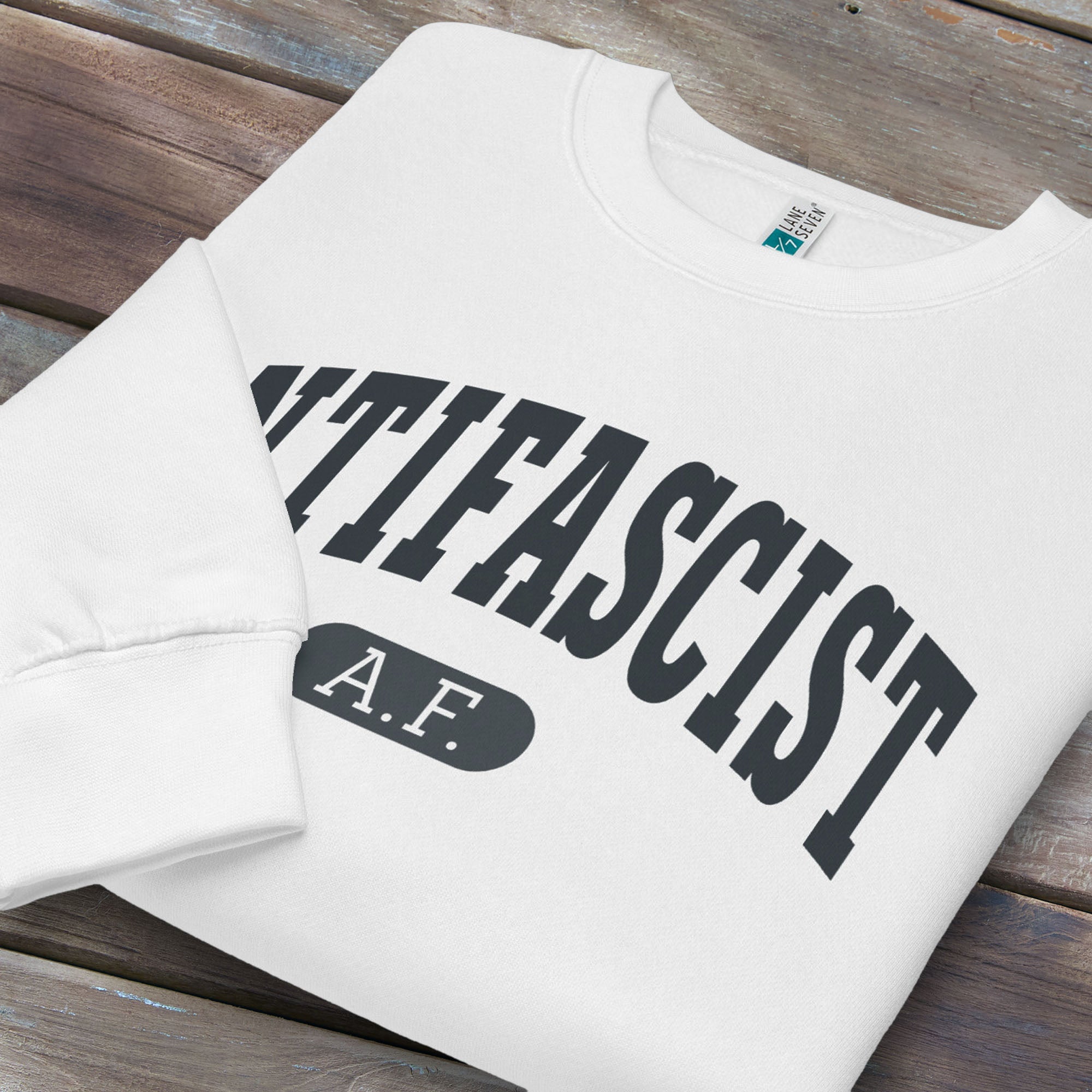Folded white crewneck sweatshirt with varsity collegiate style text across the front that reads "Antifascist AF."