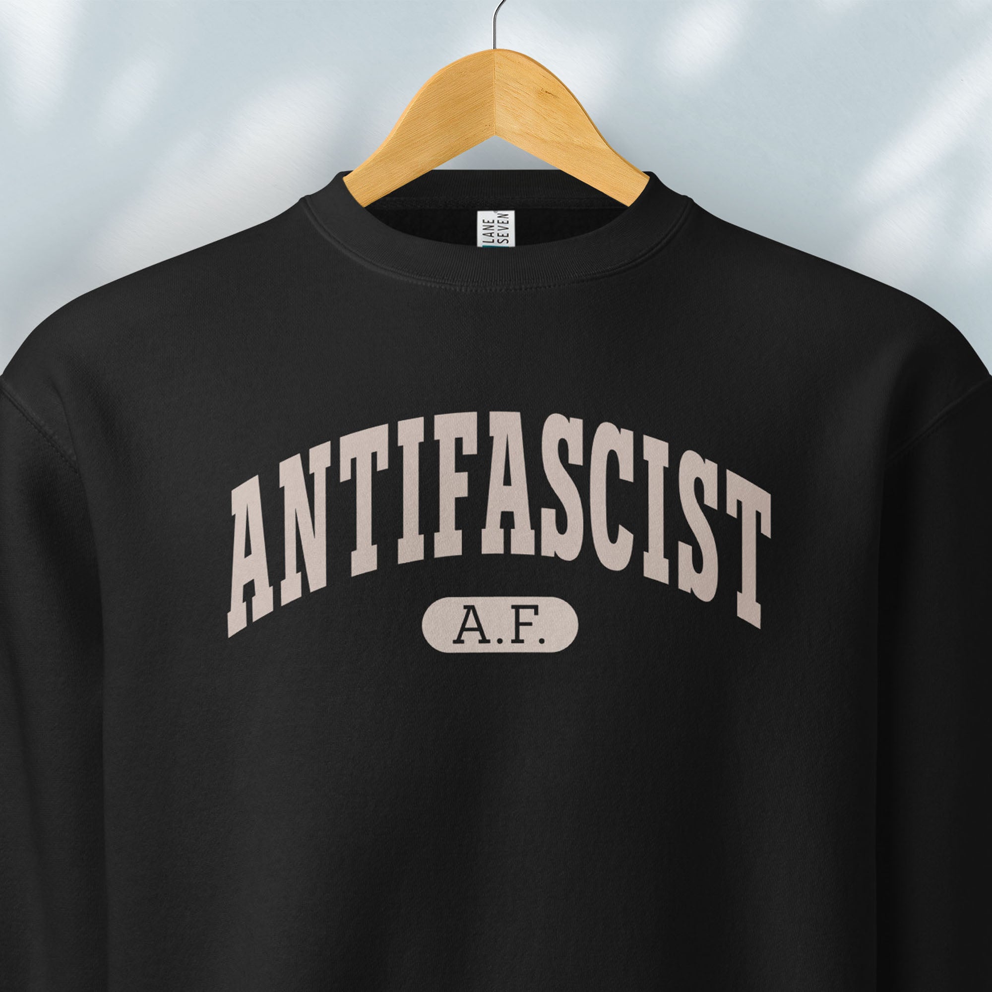 Hanging black crewneck sweatshirt with varsity collegiate style text across the front that reads "Antifascist AF."