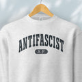 Hanging grey crewneck sweatshirt with varsity collegiate style text across the front that reads "Antifascist AF."