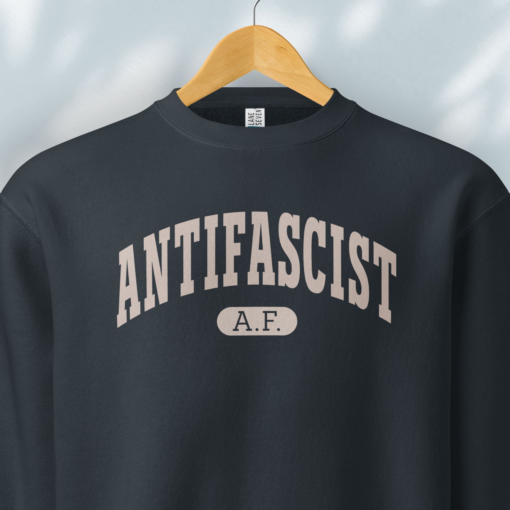 Hanging navy crewneck sweatshirt with varsity collegiate style text across the front that reads "Antifascist AF."
