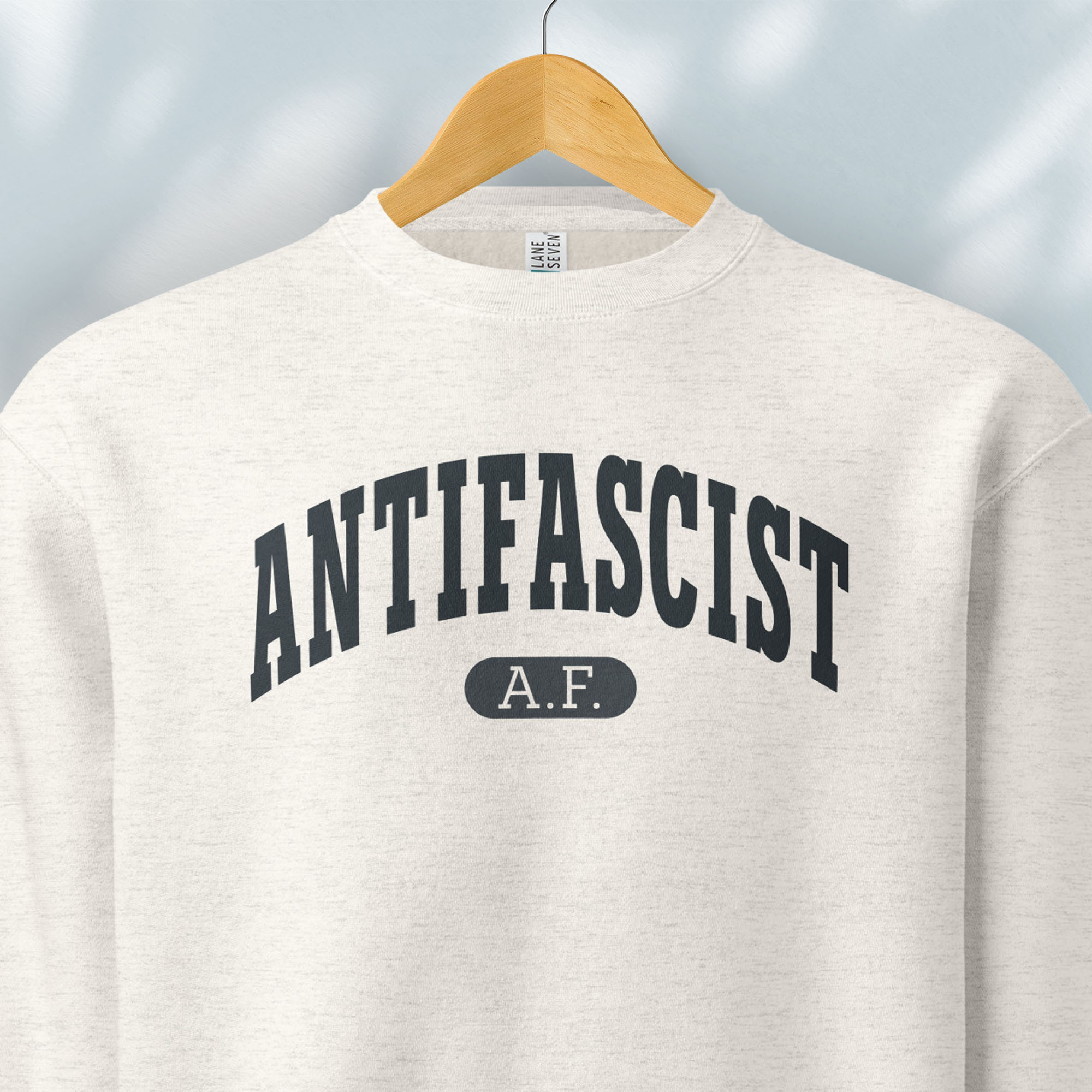 Hanging oatmeal crewneck sweatshirt with varsity collegiate style text across the front that reads "Antifascist AF."