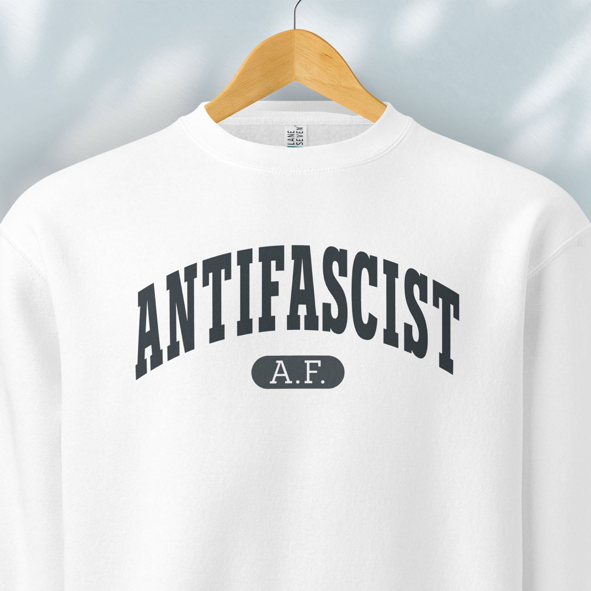Hanging white crewneck sweatshirt with varsity collegiate style text across the front that reads "Antifascist AF."