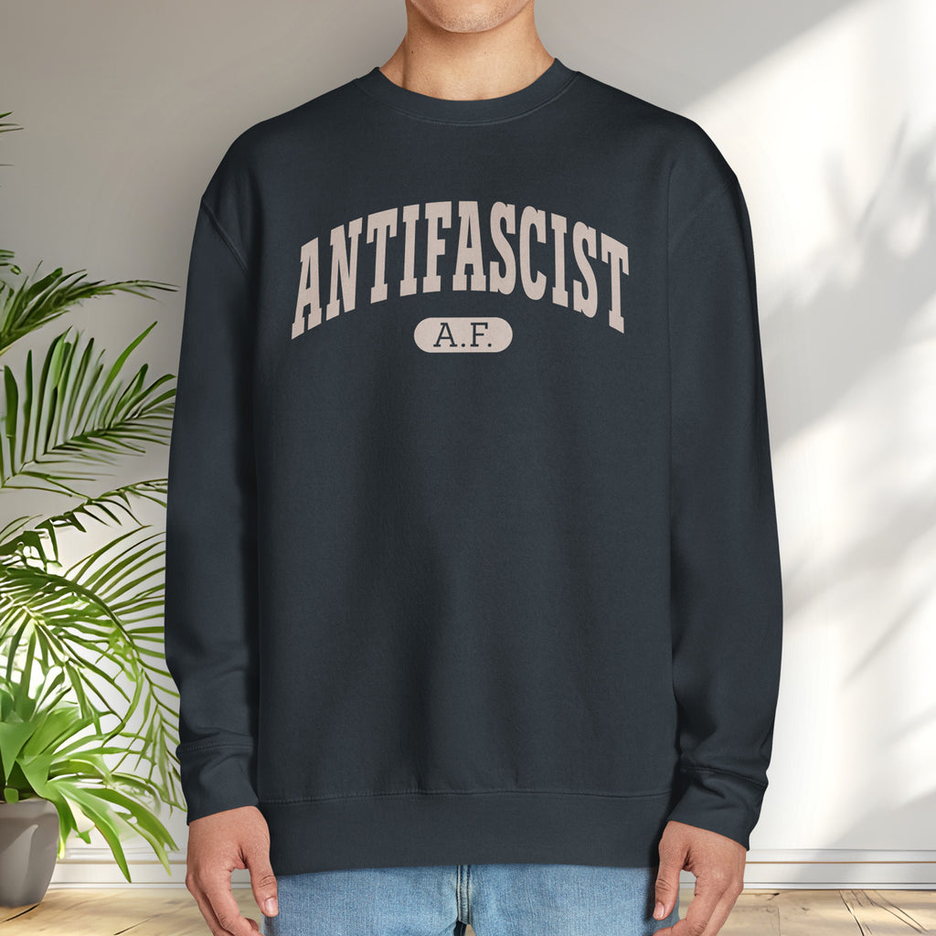 Male model wearing navy crewneck sweatshirt with varsity collegiate style text across the front that reads "Antifascist AF."