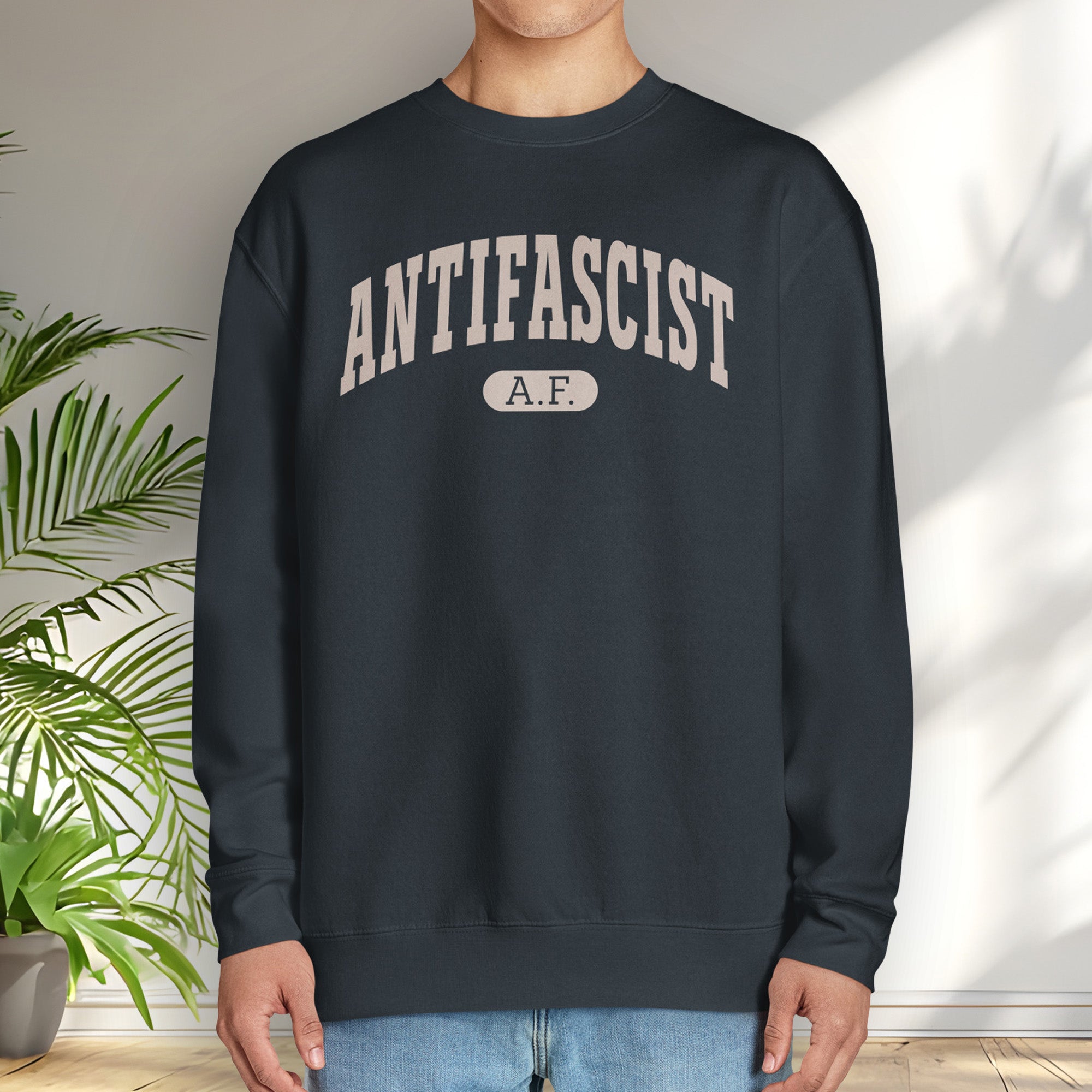 Male model wearing navy crewneck sweatshirt with varsity collegiate style text across the front that reads "Antifascist AF."