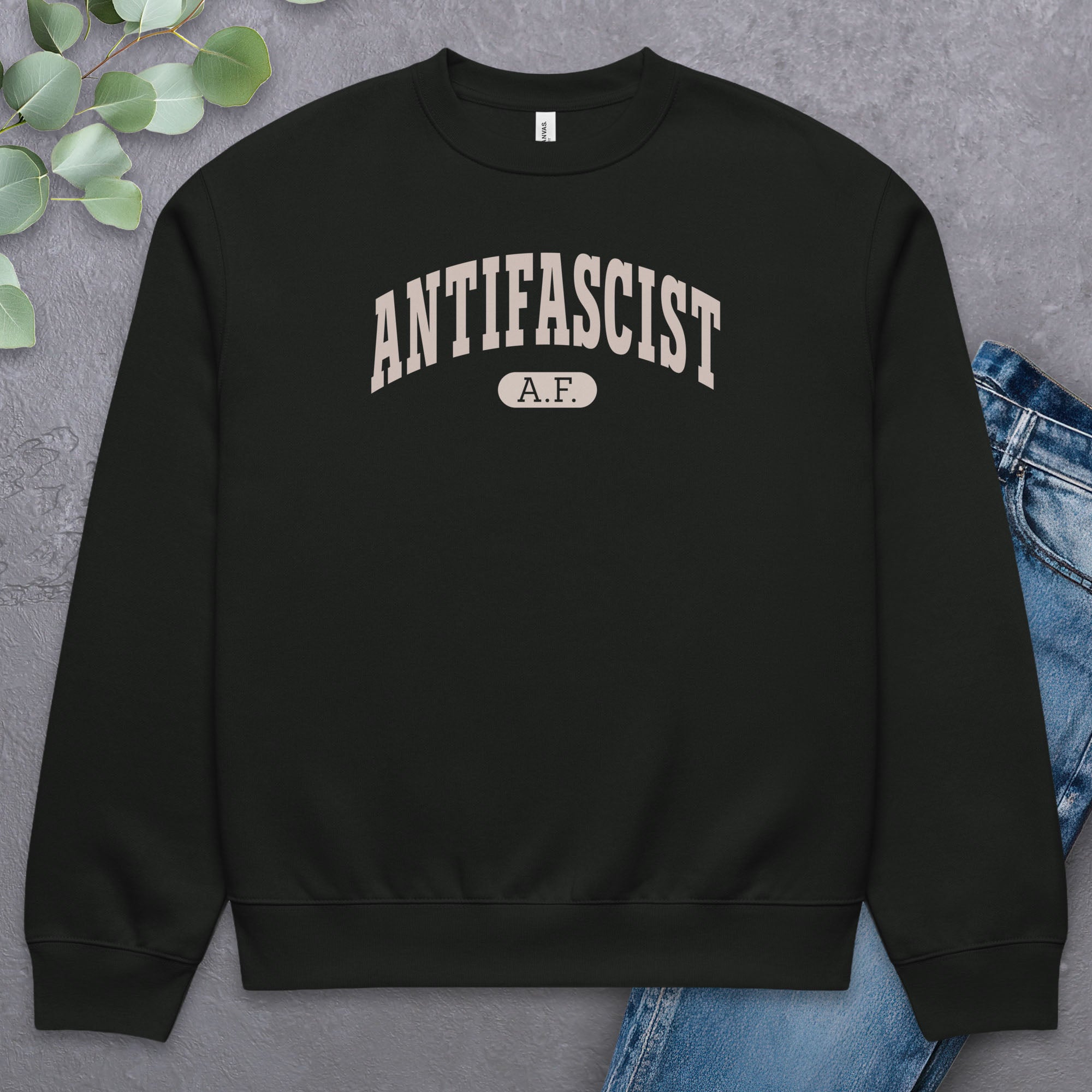 Flat black Bella + Canvas heavyweight crewneck sweatshirt with varsity collegiate style text across the front that reads "Antifascist AF." Style with greenery and a pair of jeans.