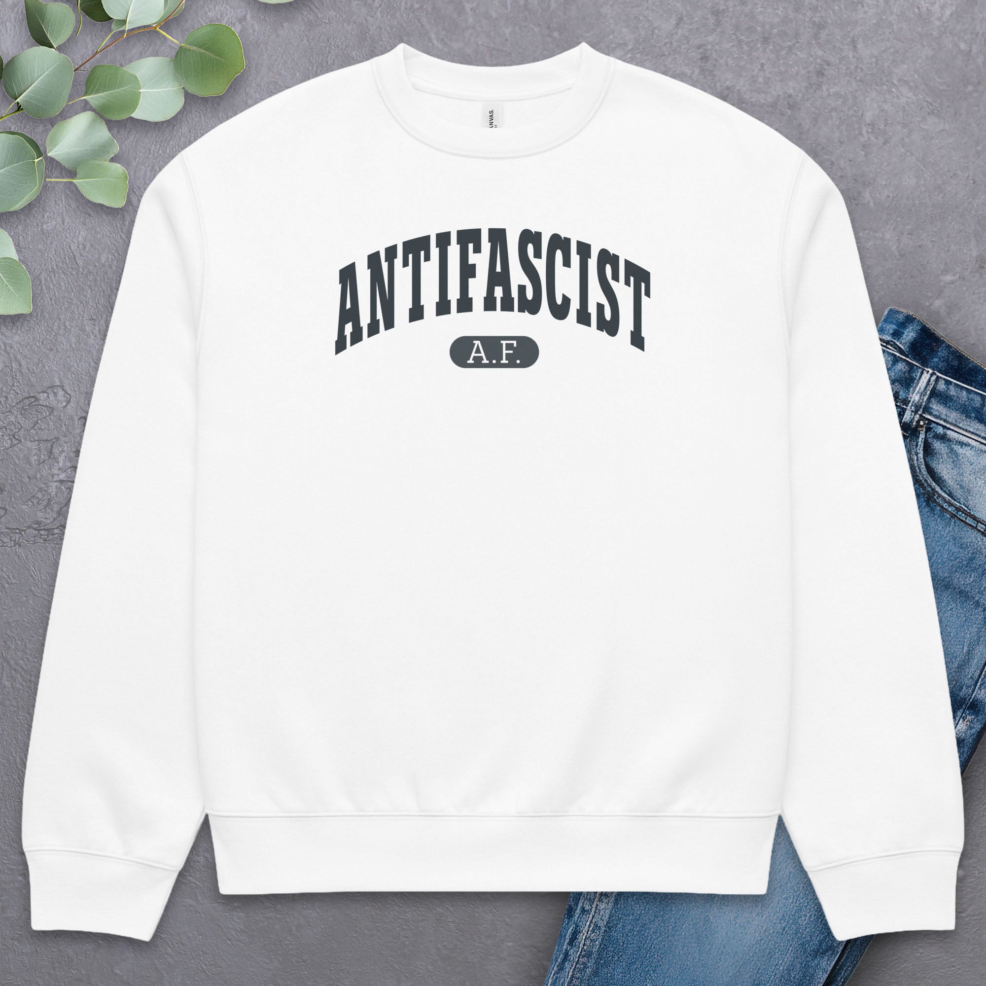Flat white Bella + Canvas heavyweight crewneck sweatshirt with varsity collegiate style text across the front that reads "Antifascist AF." Style with greenery and a pair of jeans.