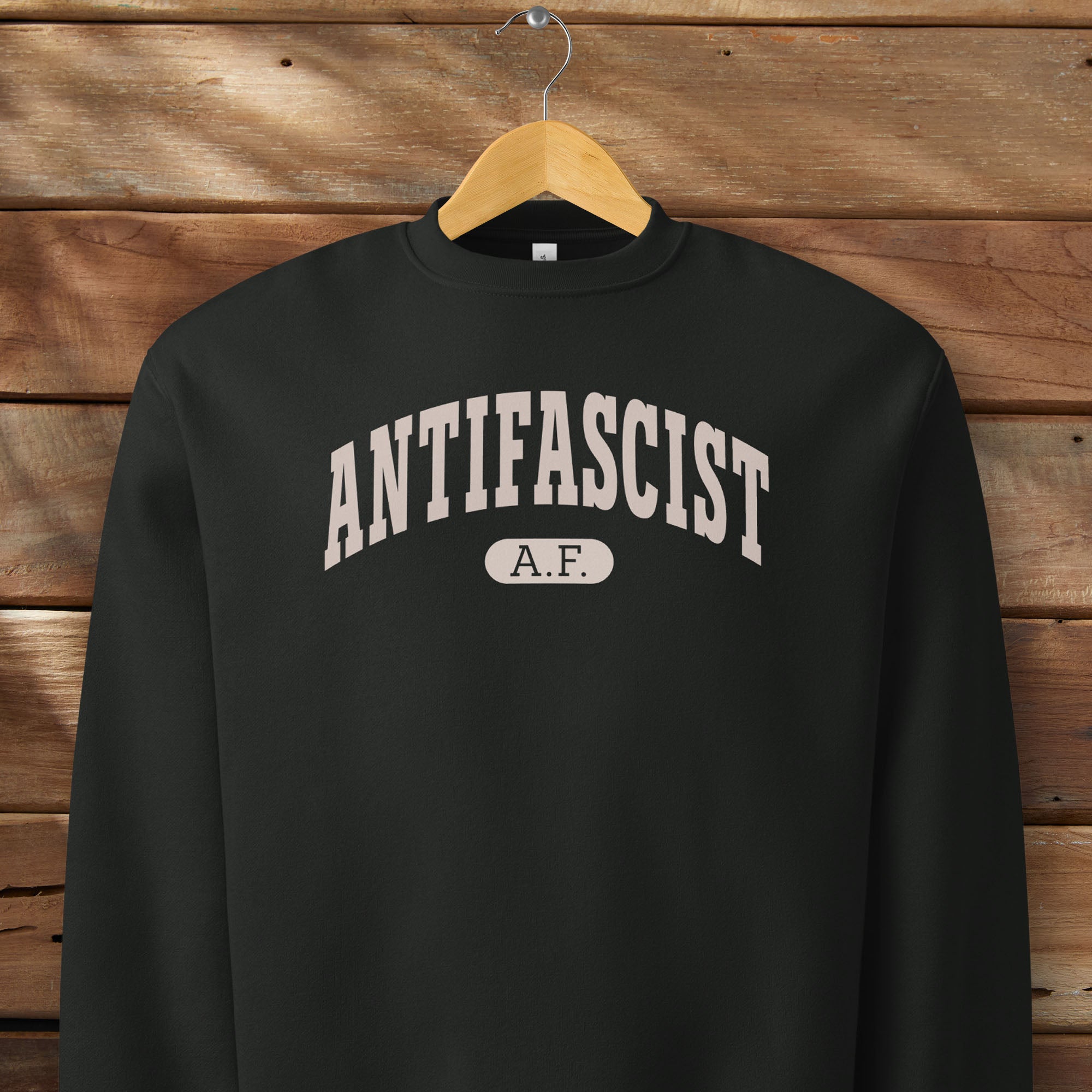 Hanging black Bella + Canvas heavyweight crewneck sweatshirt with varsity collegiate style text across the front that reads "Antifascist AF."