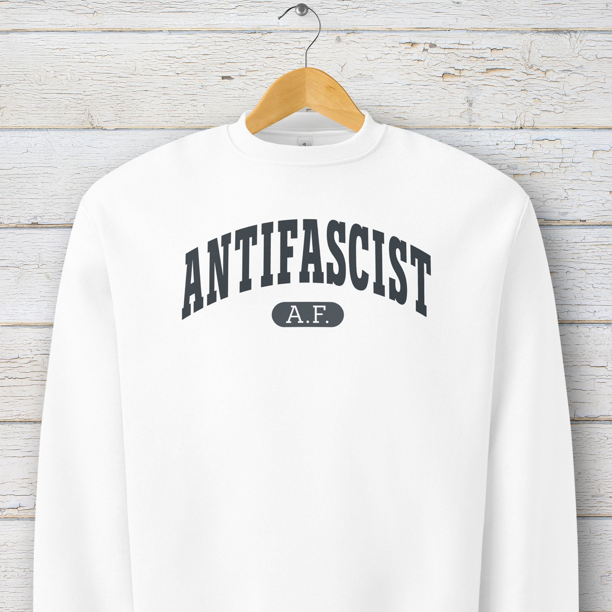 Hanging white Bella + Canvas heavyweight crewneck sweatshirt with varsity collegiate style text across the front that reads "Antifascist AF."