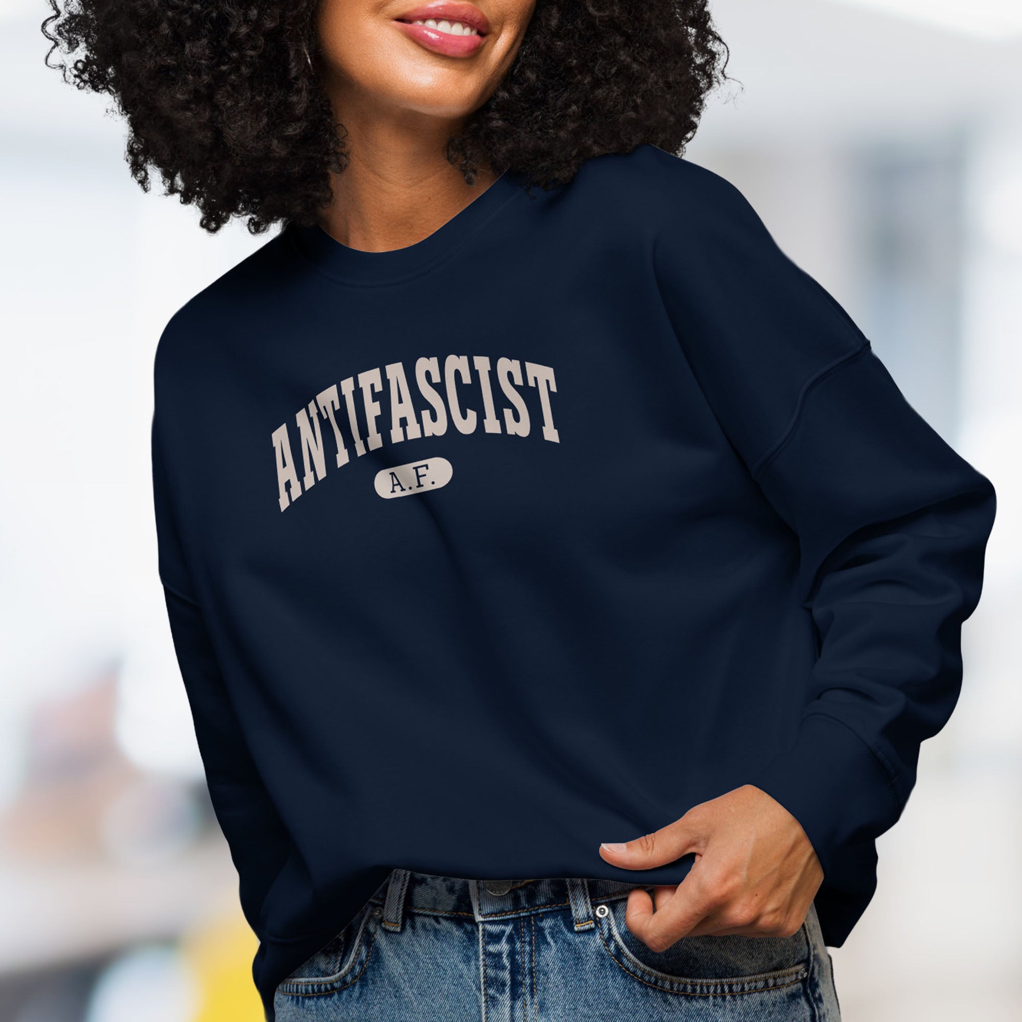 Front view of female model wearing navy sweatshirt with greyish tan text that reads “Antifascist A.F.” in a collegiate style.