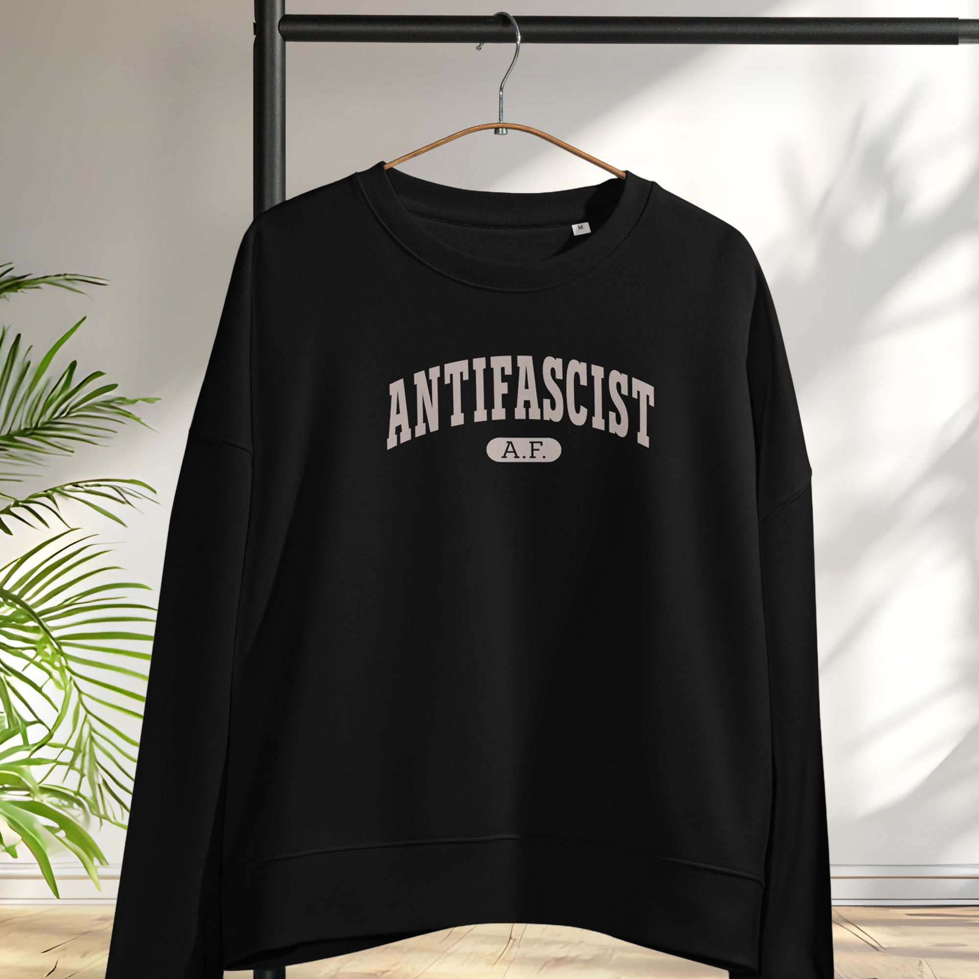 Hanging black sweatshirt with greyish tan text that reads “Antifascist A.F.” in a collegiate style.