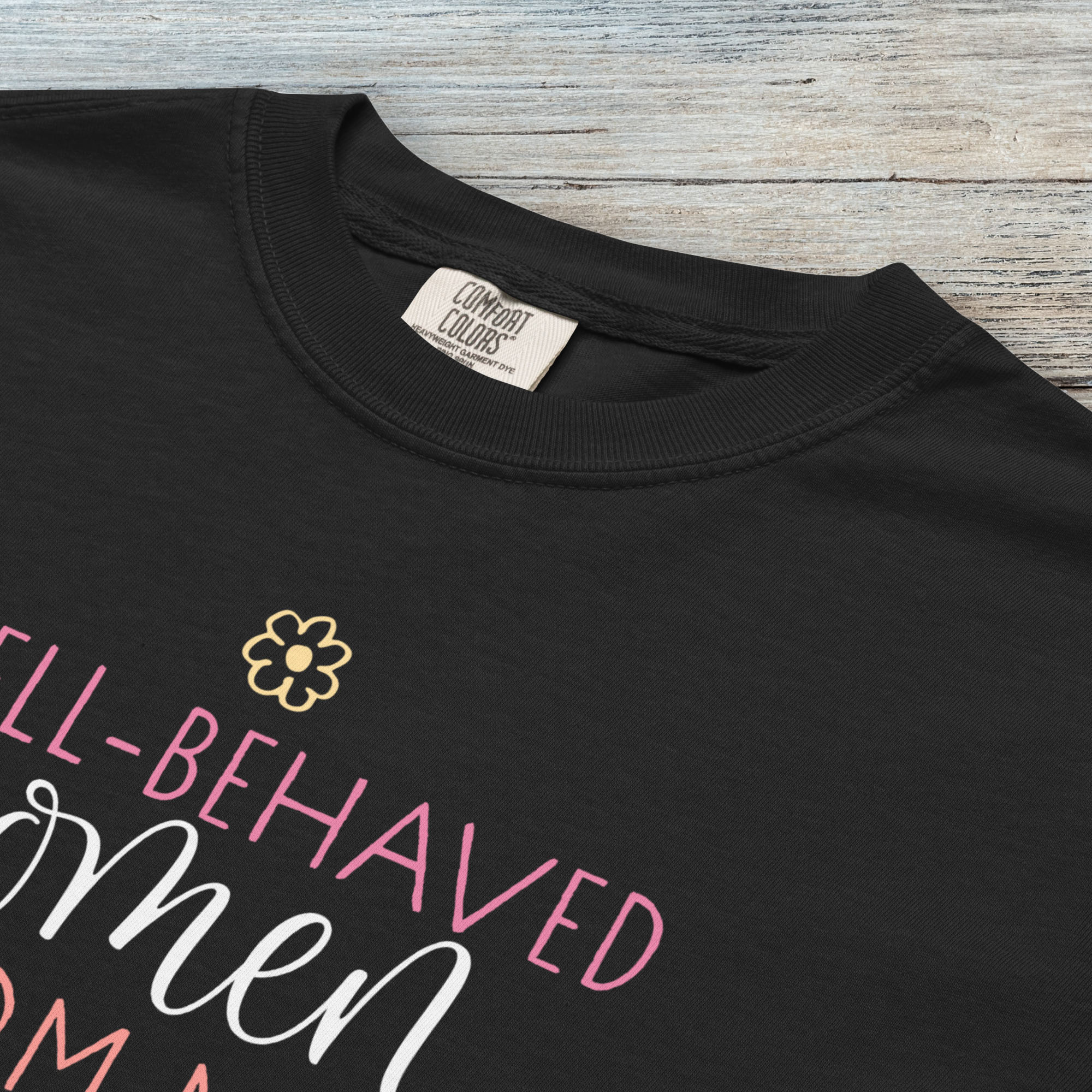 Closeup detail of black feminist t-shirt with colorful text that reads “Well-behaved women seldom make history” — empowering women’s rights shirt and activist apparel.