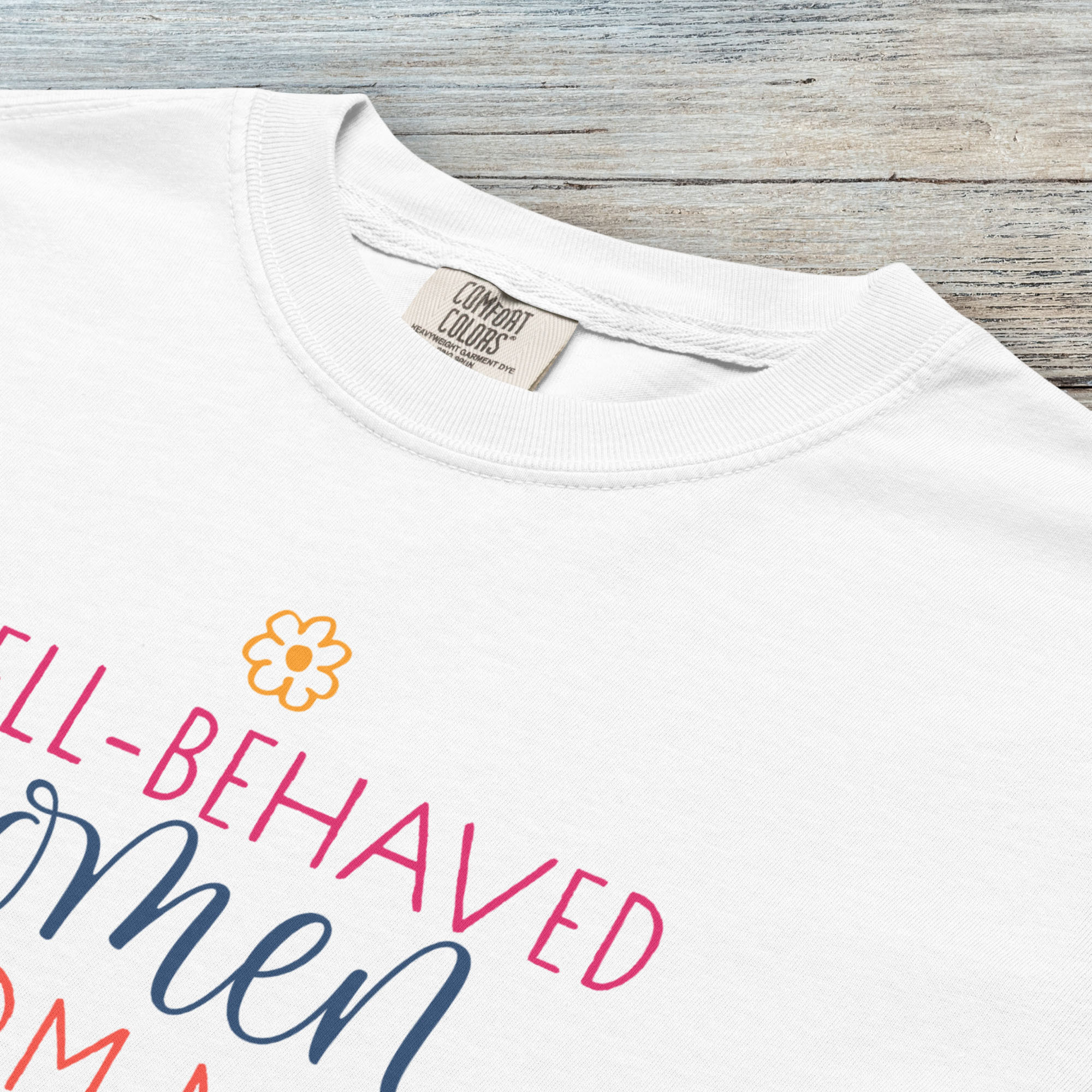 Closeup detail of white feminist t-shirt with colorful text that reads “Well-behaved women seldom make history” — empowering women’s rights shirt and activist apparel.