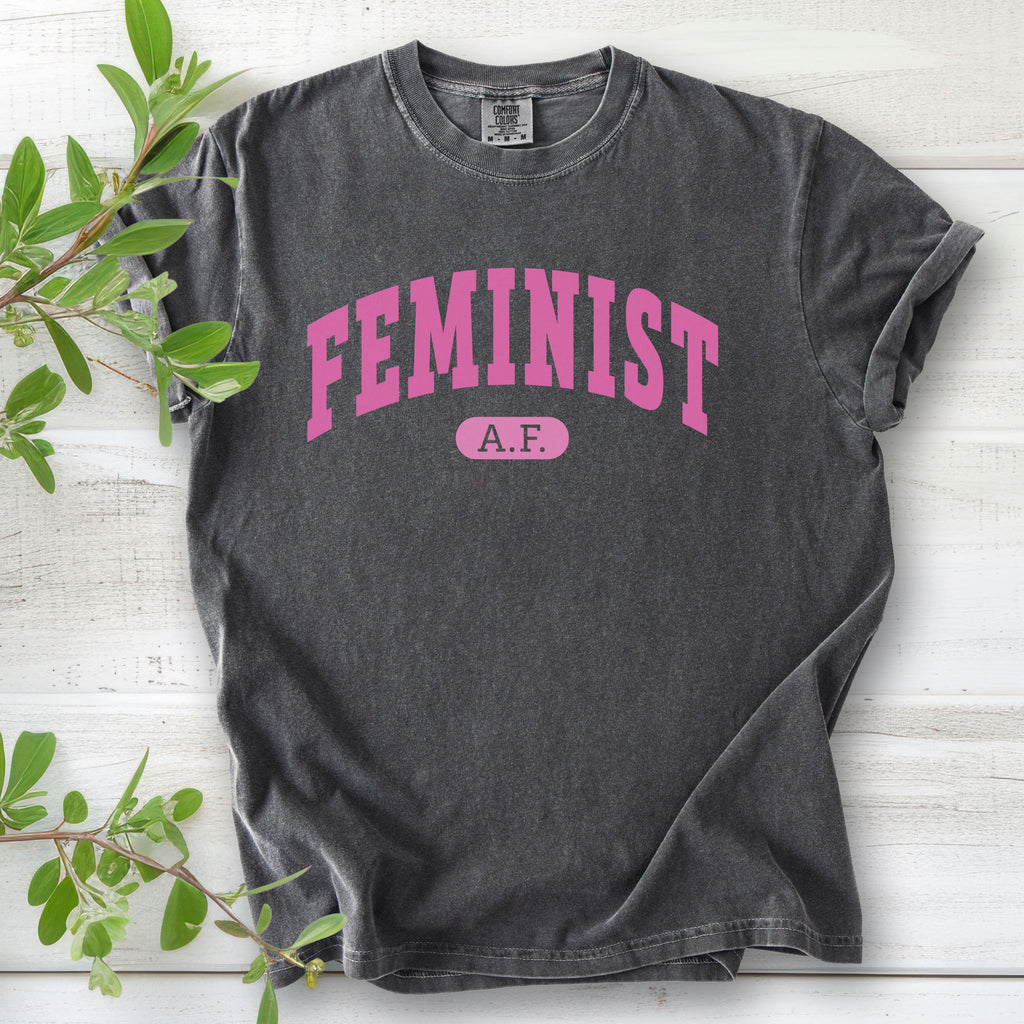 Pepper grey Comfort Colors tee with pink text that reads “Feminist A.F.” in a collegiate style.