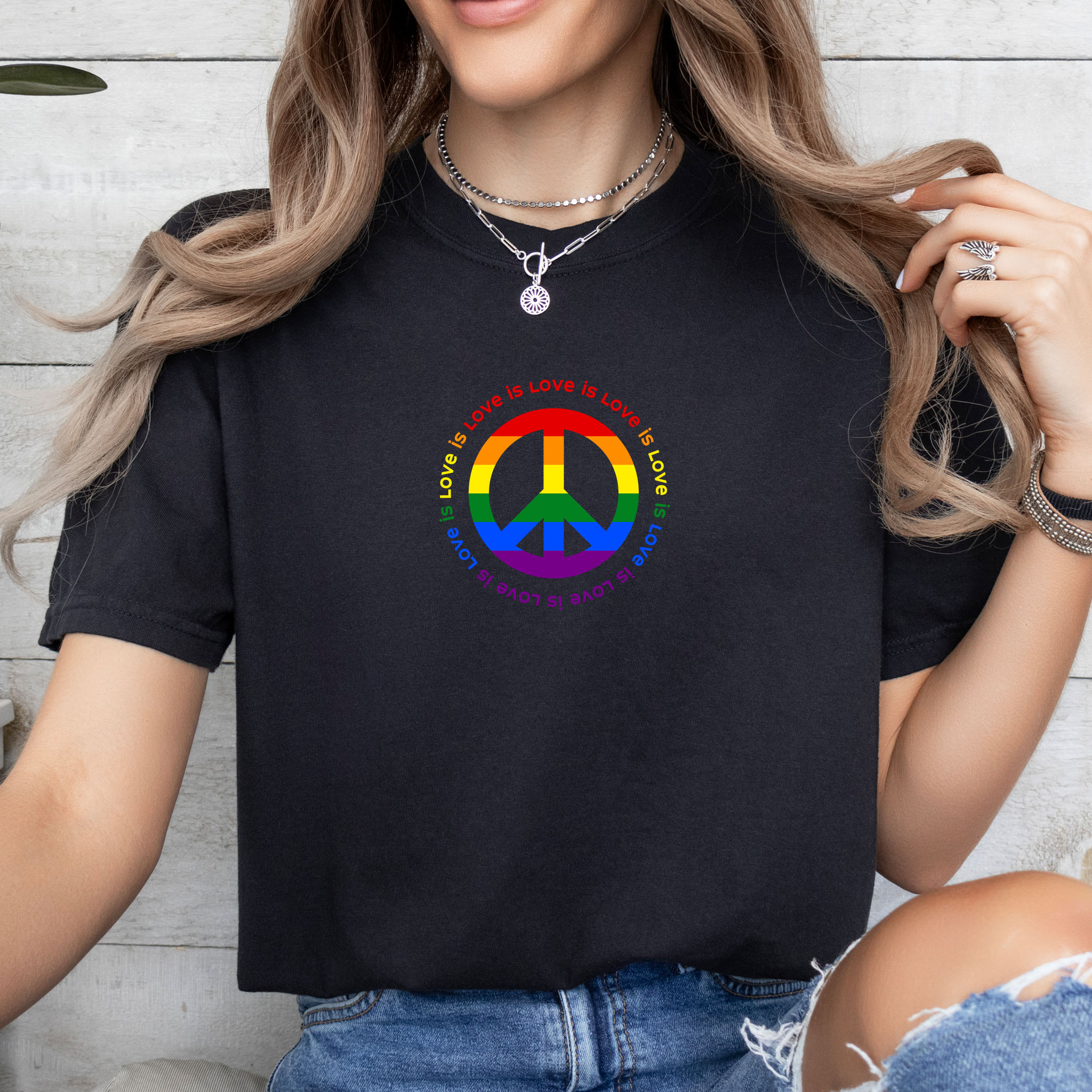Female model wearing t-shirt with LGBTQ pride graphic — a peace sign in the LGBTQ flag colors, with the text "love is love" repeated in a circle around the peace sign.
