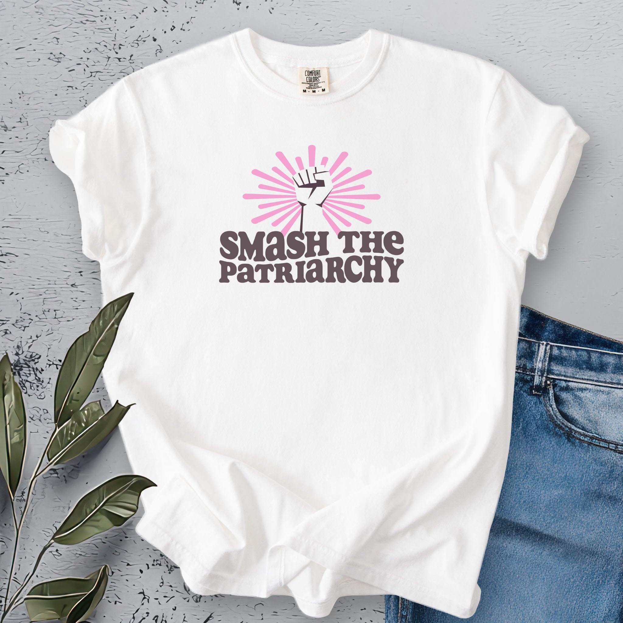 White t-shirt with a raised fist graphic and pink rays behind it, featuring the text “Smash the Patriarchy.”