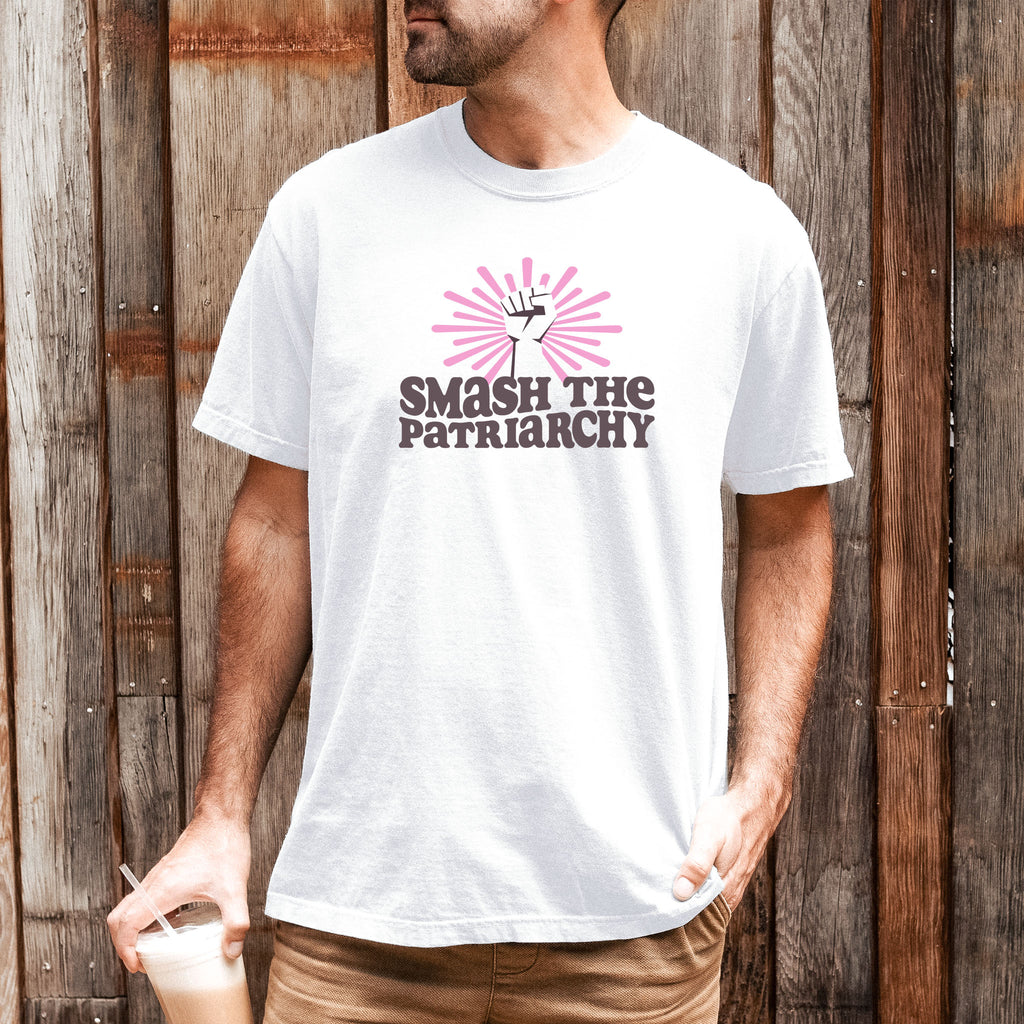 Male model wearing white t-shirt with a raised fist graphic and pink rays behind it, featuring the text “Smash the Patriarchy.”