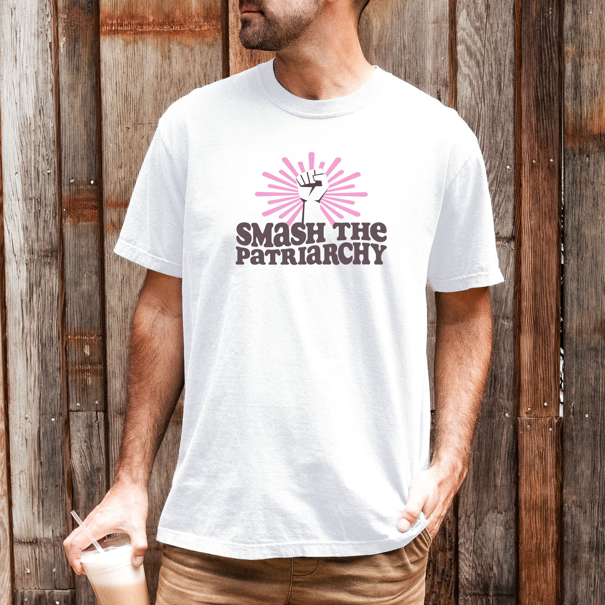 Male model wearing white t-shirt with a raised fist graphic and pink rays behind it, featuring the text “Smash the Patriarchy.”