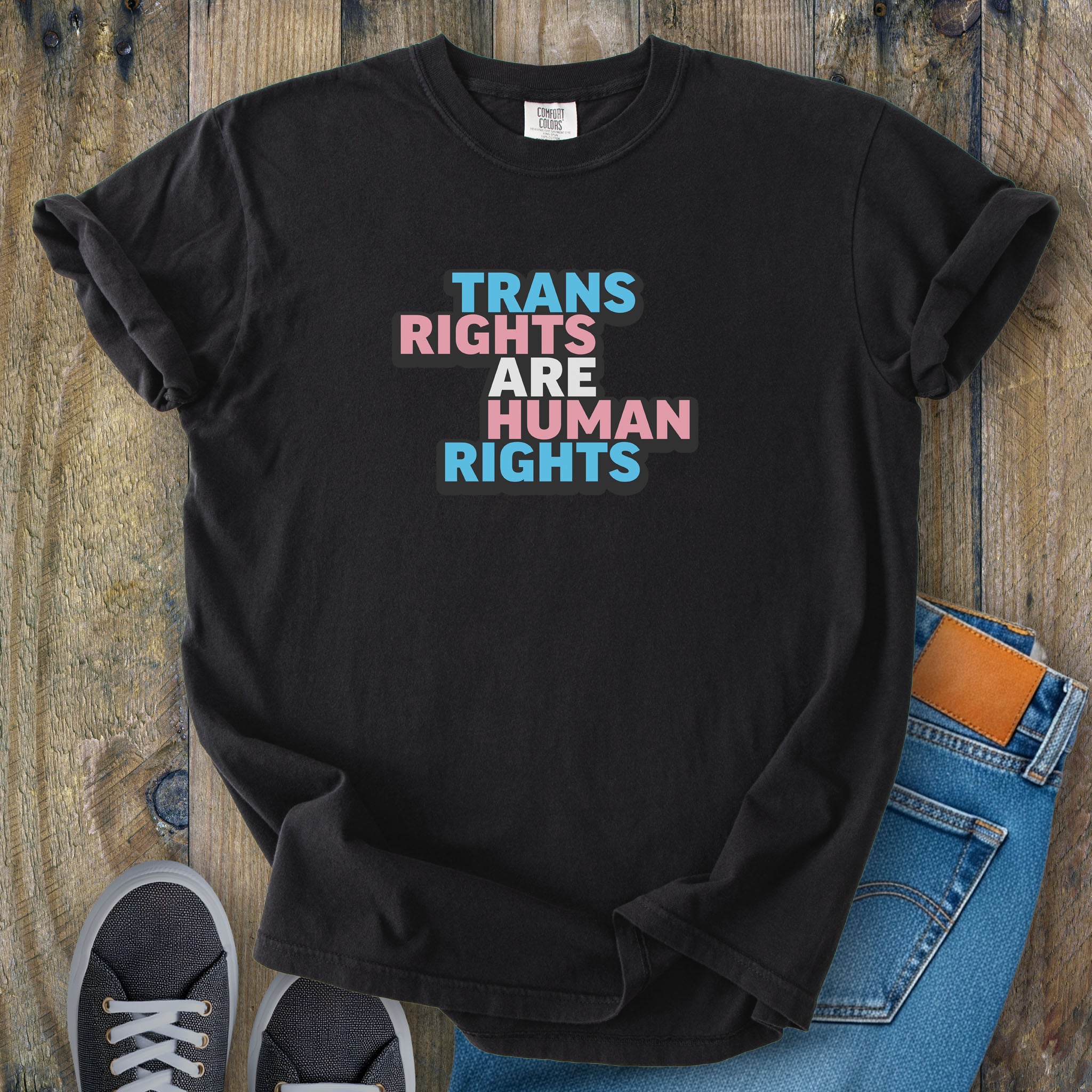 Black t-shirt with graphic that reads "trans rights are human rights" in the light blue, pink, and white colors of the trans flag, with a black shadow outlining the text.