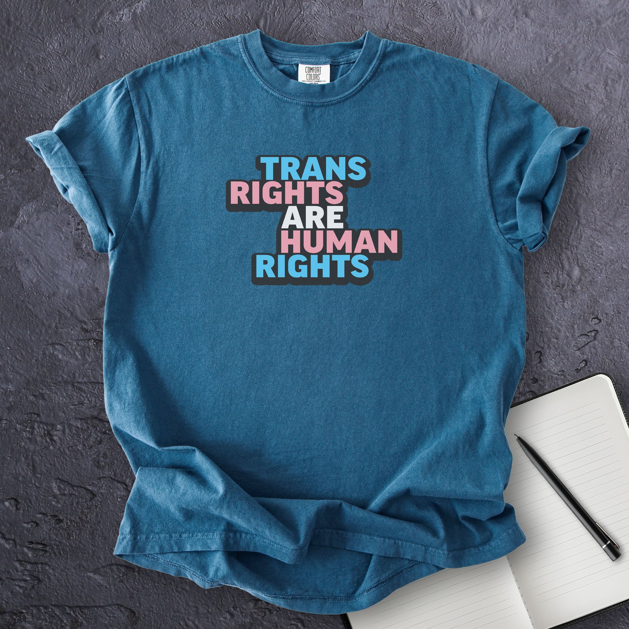 Midnight blue t-shirt with graphic that reads "trans rights are human rights" in the light blue, pink, and white colors of the trans flag, with a black shadow outlining the text.