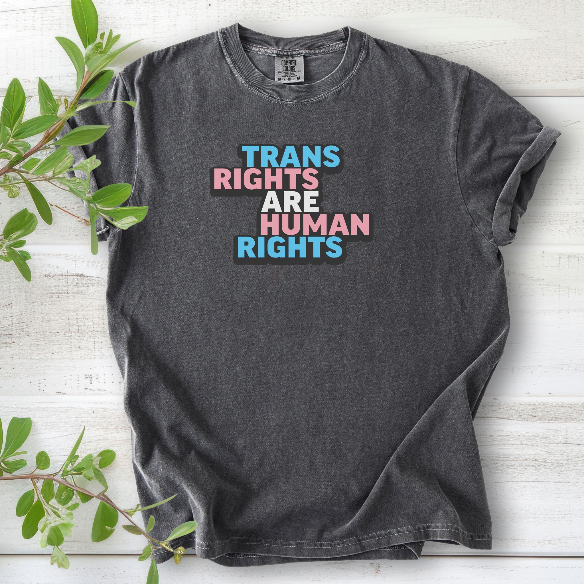Pepper gray t-shirt with graphic that reads "trans rights are human rights" in the light blue, pink, and white colors of the trans flag, with a black shadow outlining the text.