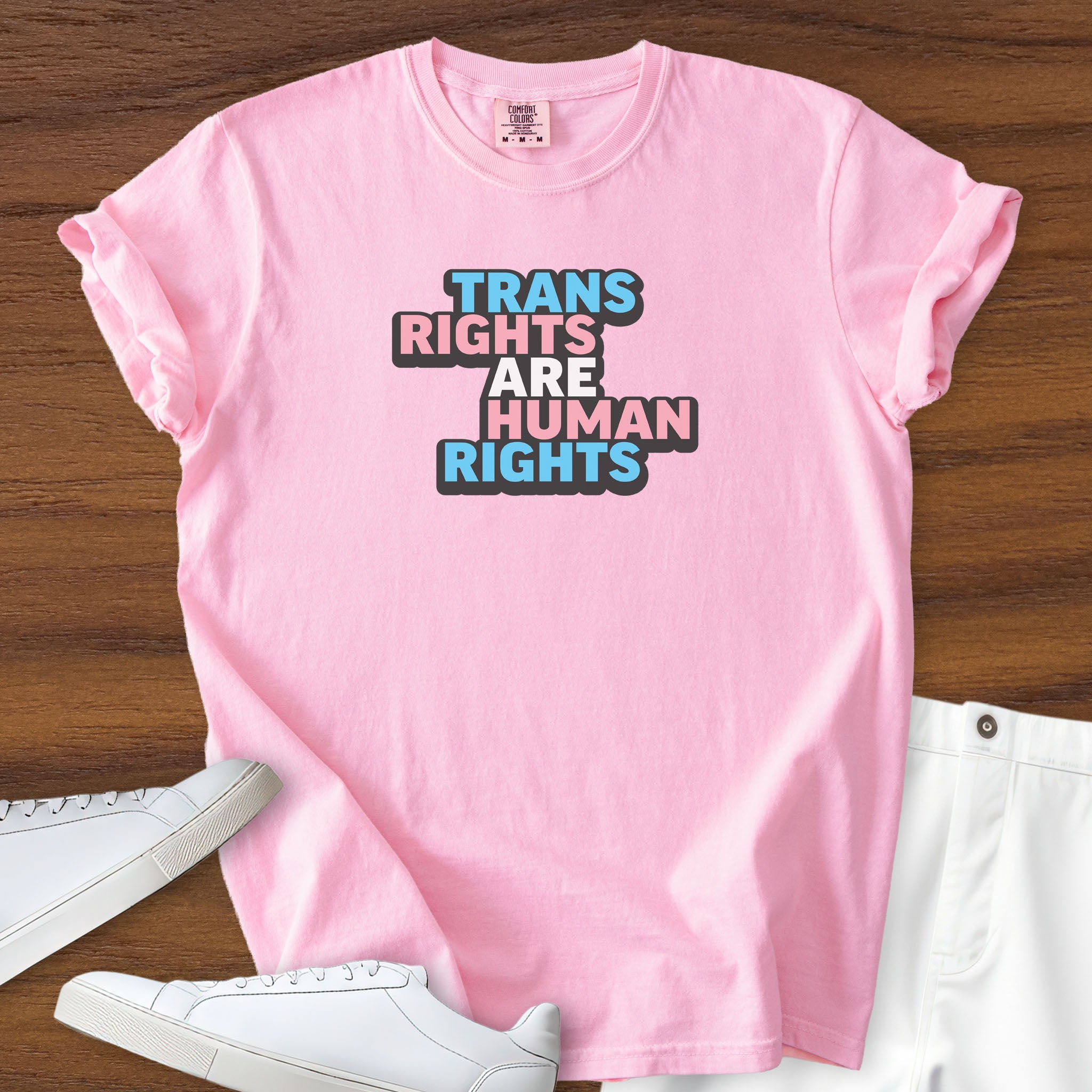 Blossom pink color t-shirt with graphic that reads &quot;trans rights are human rights&quot; in the light blue, pink, and white colors of the trans flag, with a black shadow outlining the text.