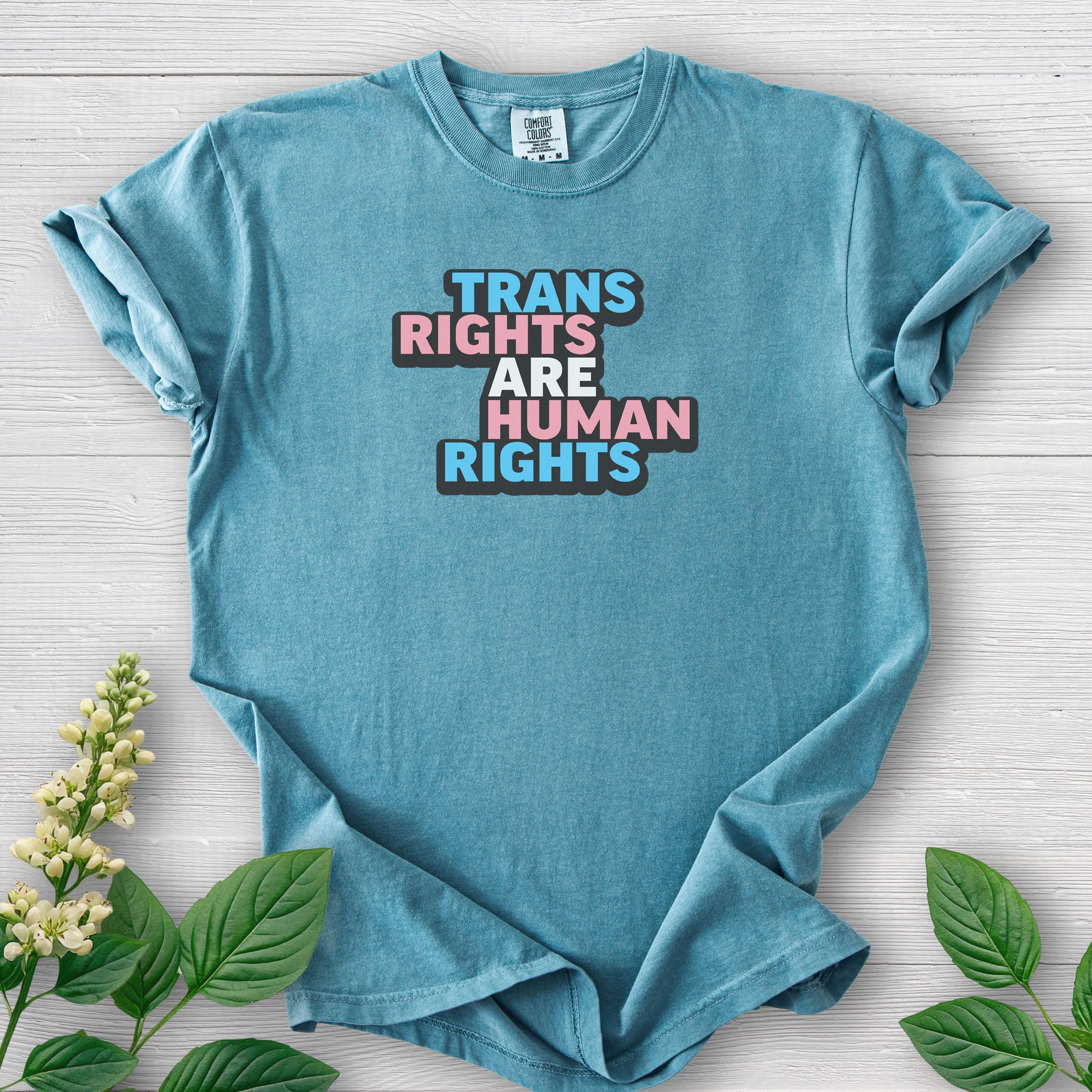 Ice blue color t-shirt with graphic that reads &quot;trans rights are human rights&quot; in the light blue, pink, and white colors of the trans flag, with a black shadow outlining the text.