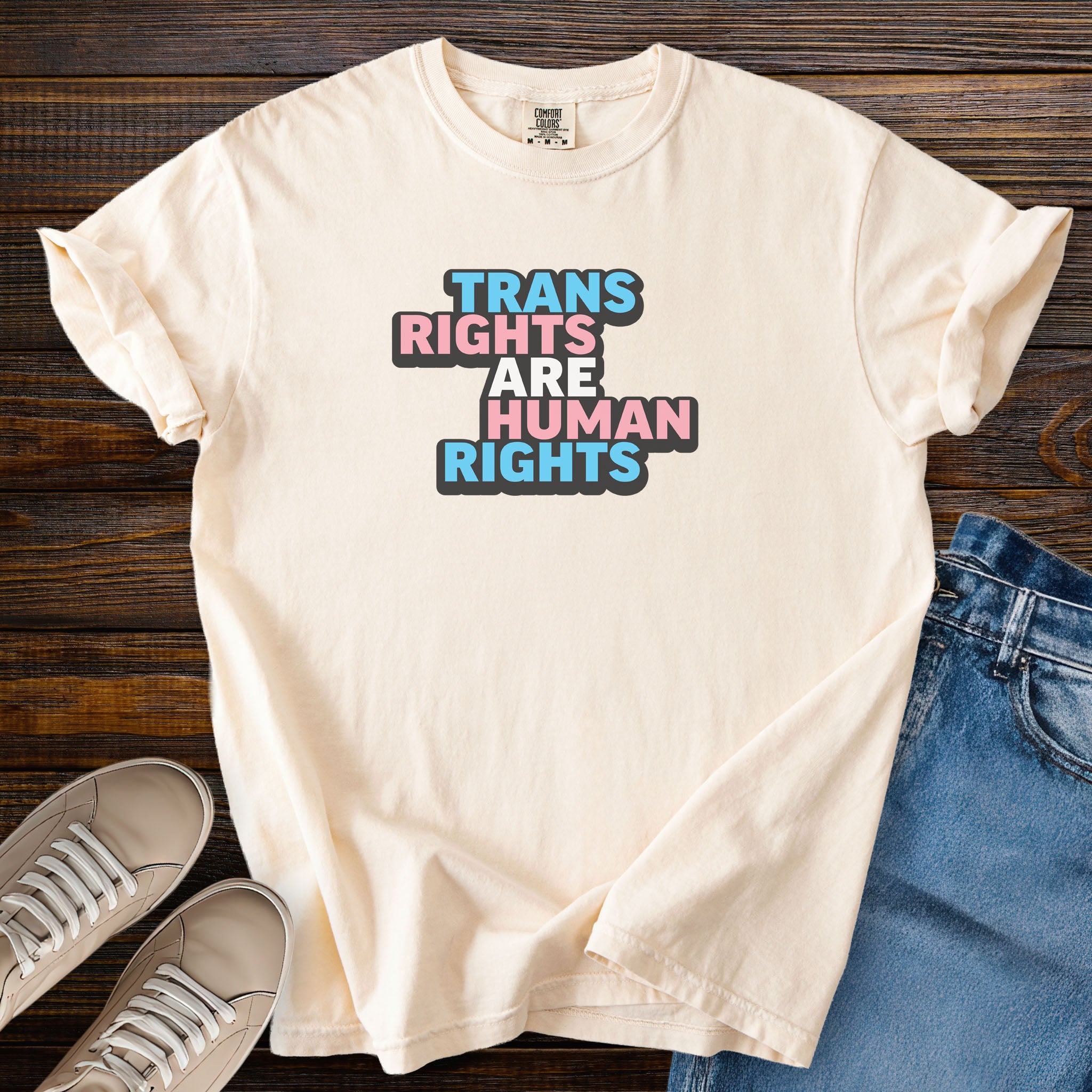 Ivory color t-shirt with graphic that reads &quot;trans rights are human rights&quot; in the light blue, pink, and white colors of the trans flag, with a black shadow outlining the text.