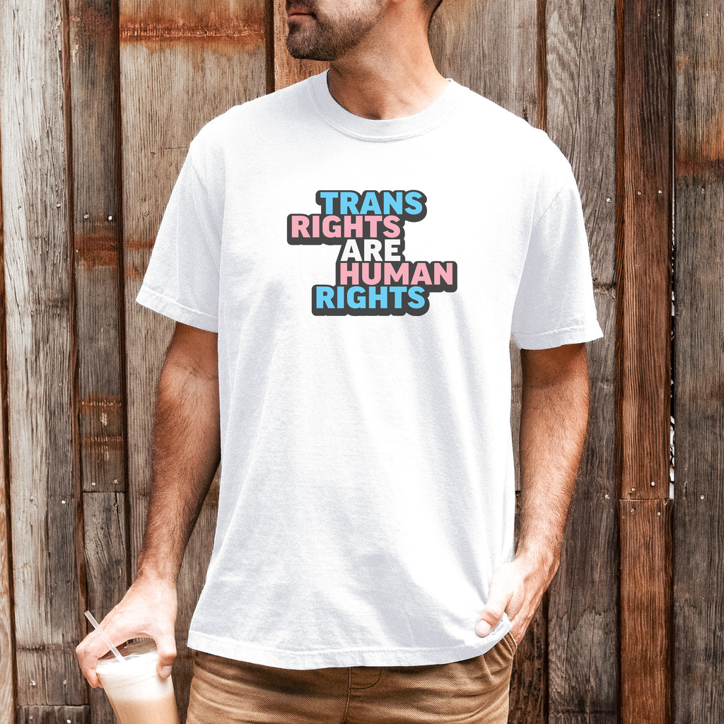Male model wearing white color t-shirt with graphic that reads &quot;trans rights are human rights&quot; in the light blue, pink, and white colors of the trans flag, with a black shadow outlining the text.