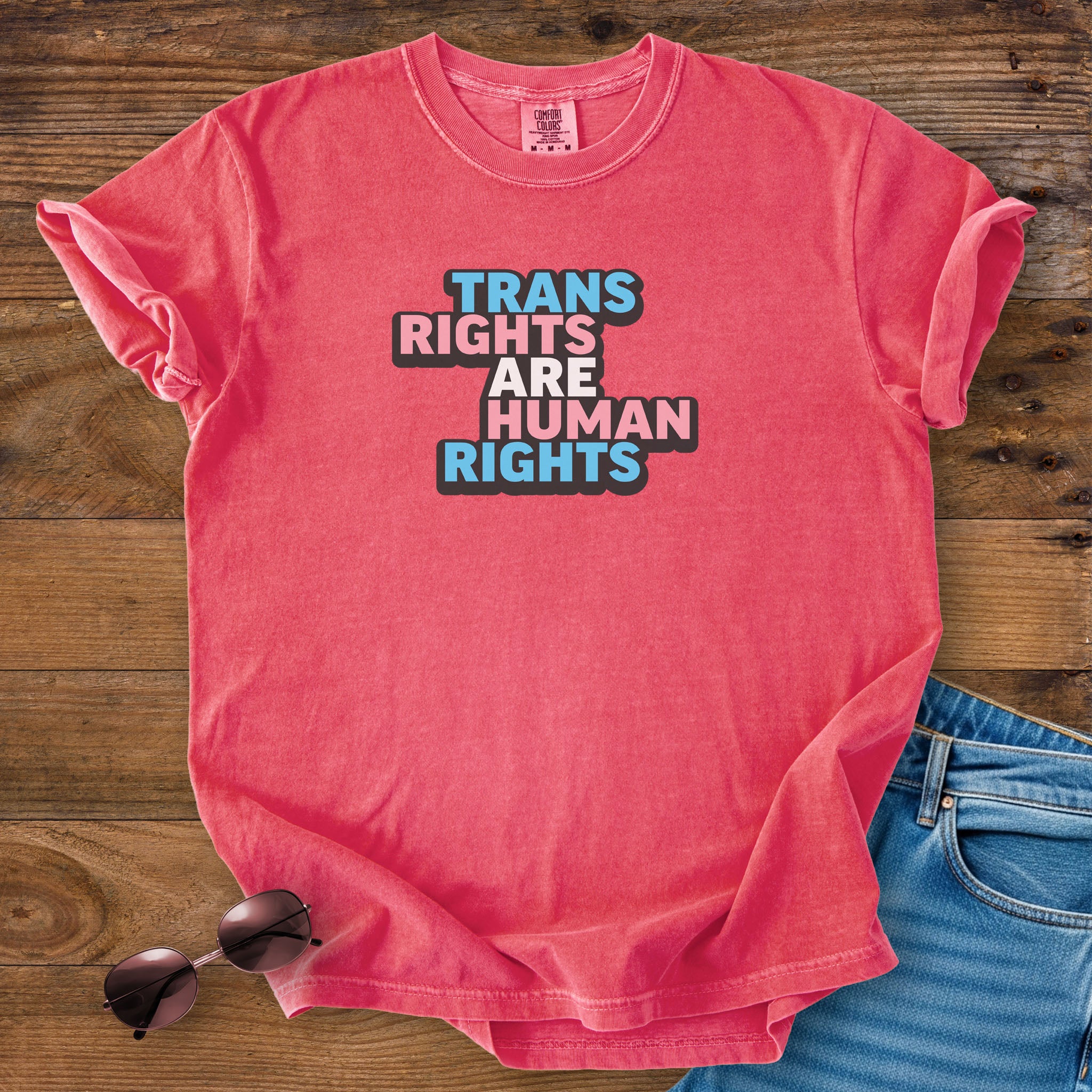 Watermelon red color t-shirt with graphic that reads &quot;trans rights are human rights&quot; in the light blue, pink, and white colors of the trans flag, with a black shadow outlining the text.