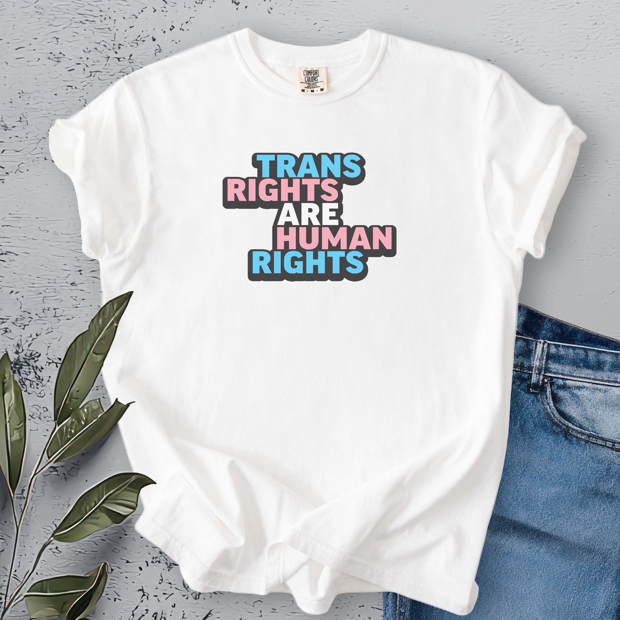 White color t-shirt with graphic that reads &quot;trans rights are human rights&quot; in the light blue, pink, and white colors of the trans flag, with a black shadow outlining the text.