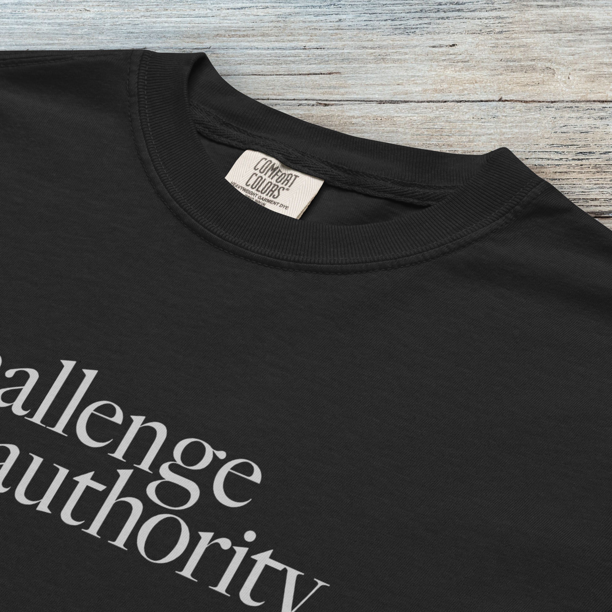 Closeup detail of black t-shirt with minimalist serif text block reading “challenge authority."