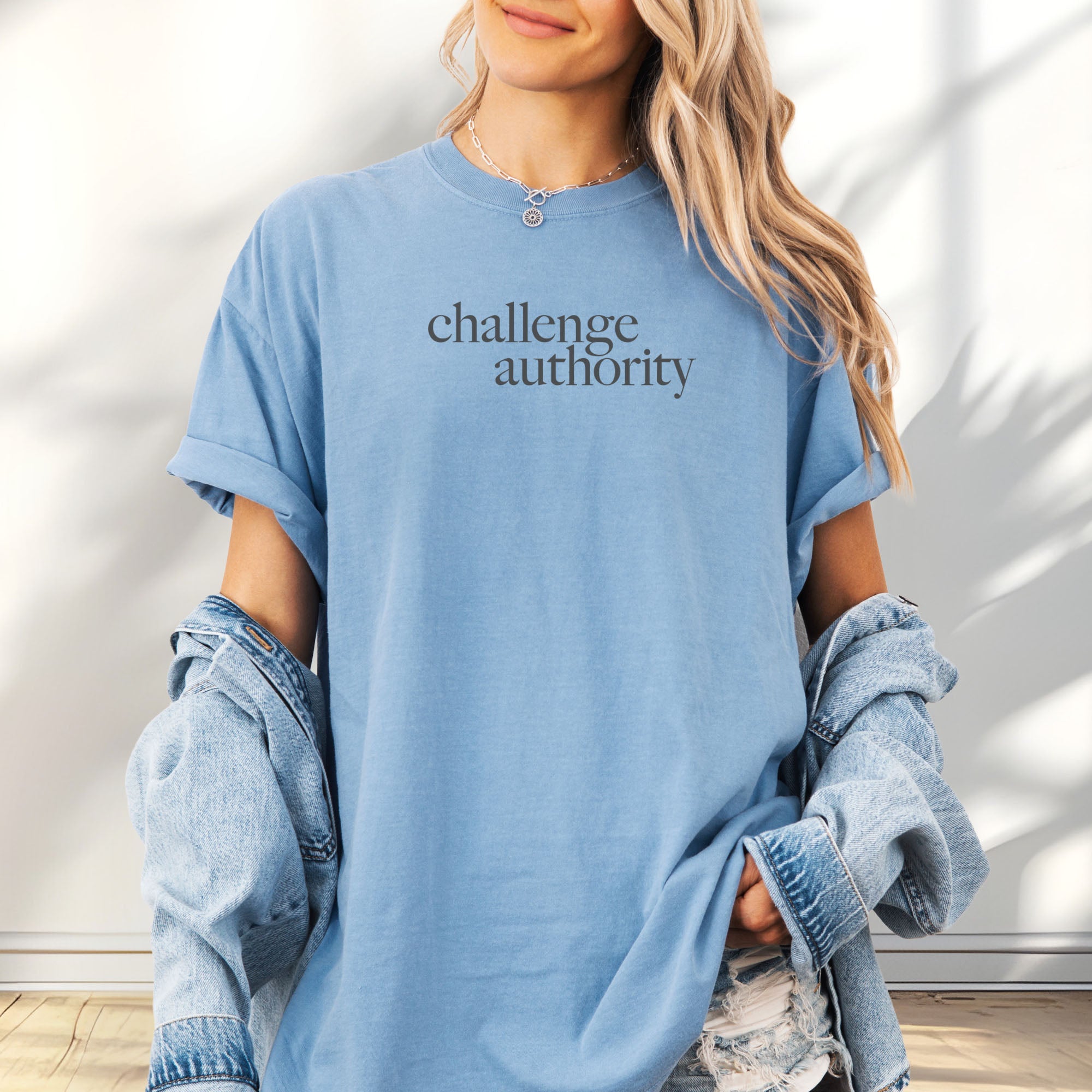 Female model wearing oversized washed denim t-shirt with minimalist serif text block reading “challenge authority."