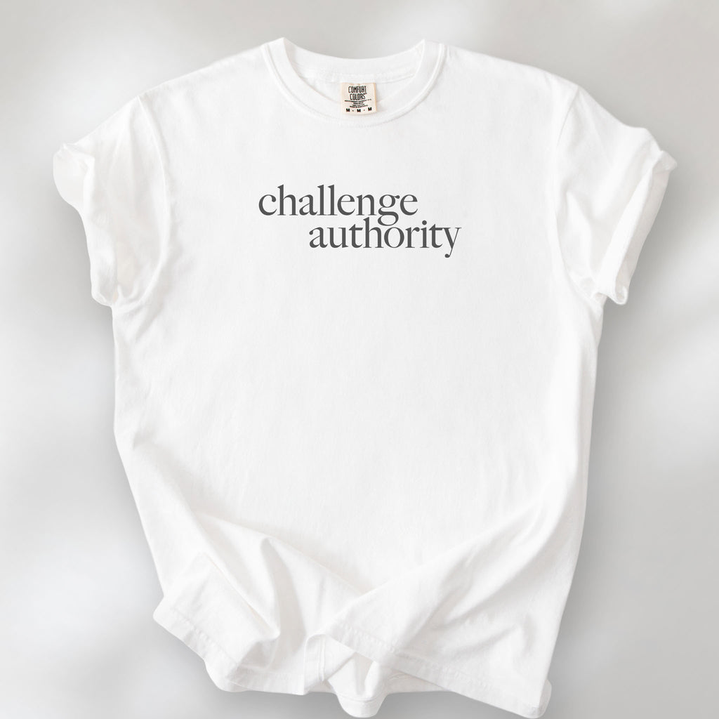 White t-shirt with minimalist serif text block reading “challenge authority."