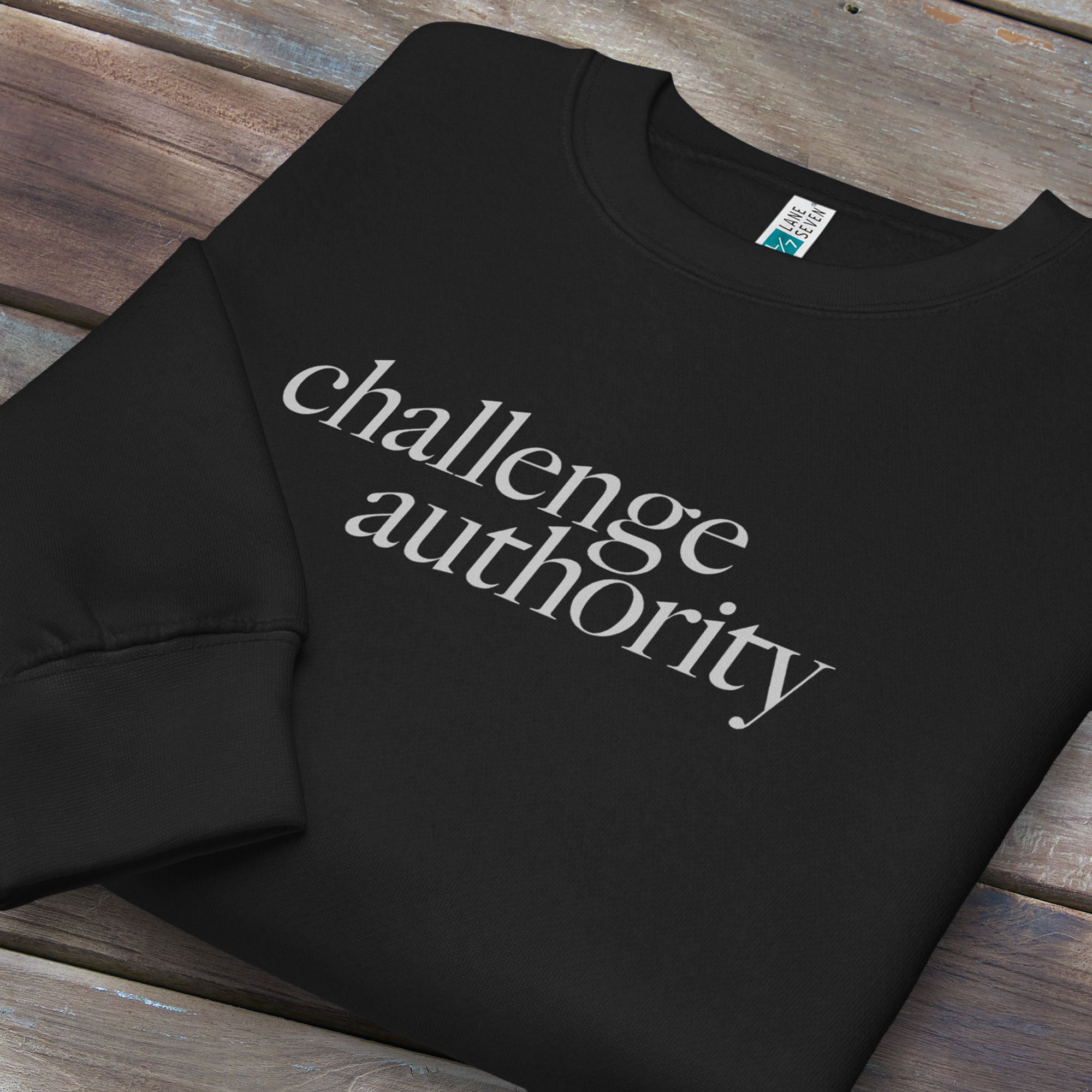 Folded black sweatshirt with minimalist serif text block reading “challenge authority."