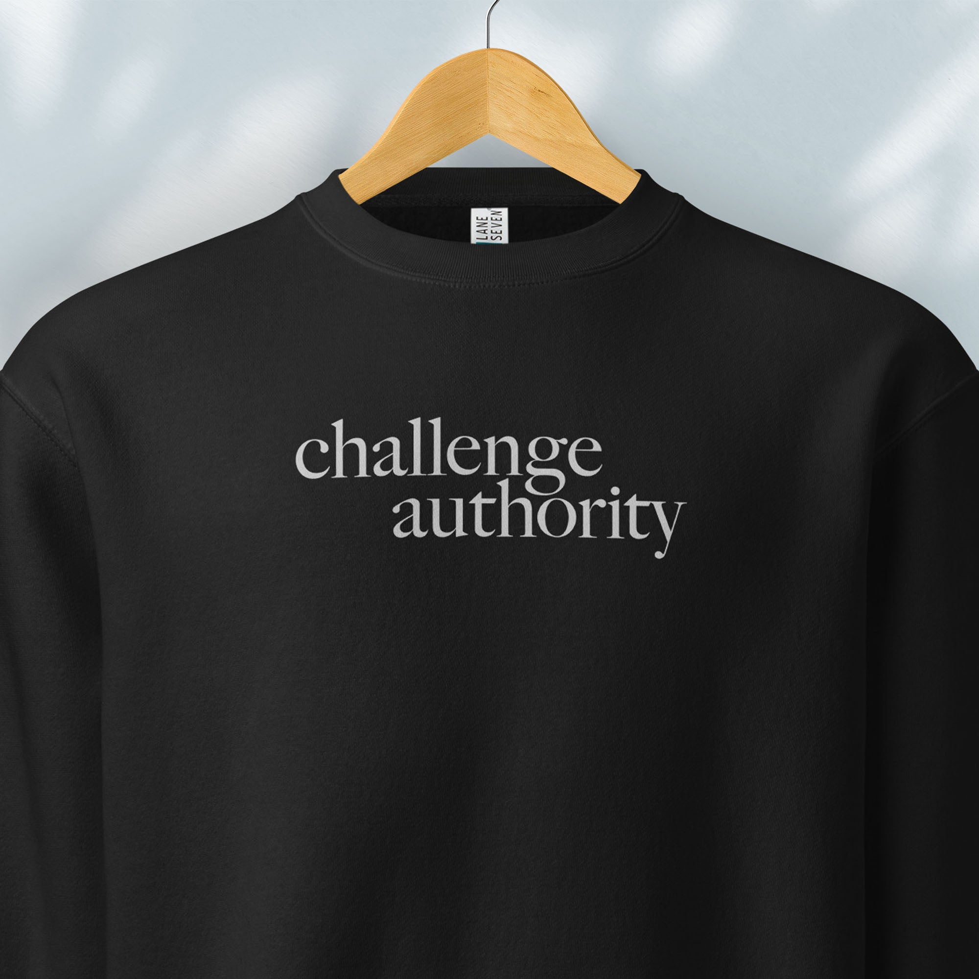 Hanging black sweatshirt with minimalist serif text block reading “challenge authority."