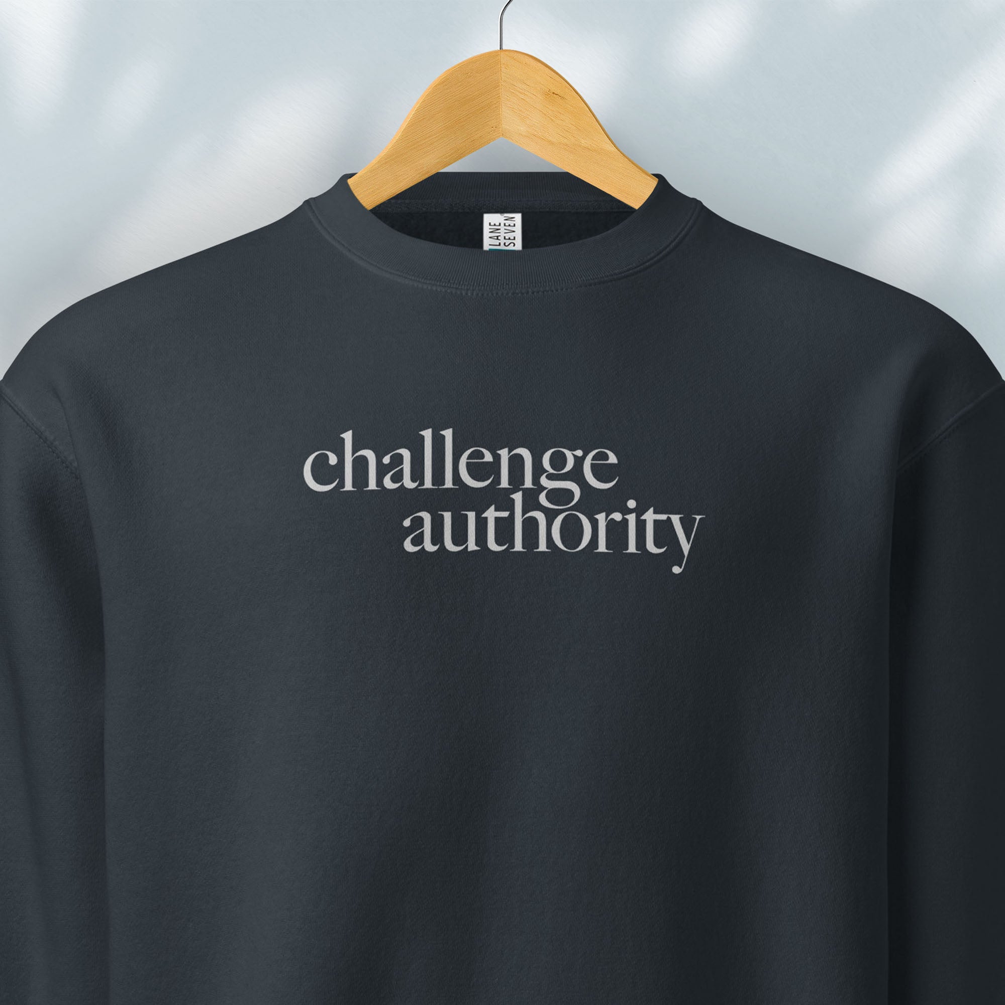 Hanging navy sweatshirt with minimalist serif text block reading “challenge authority."
