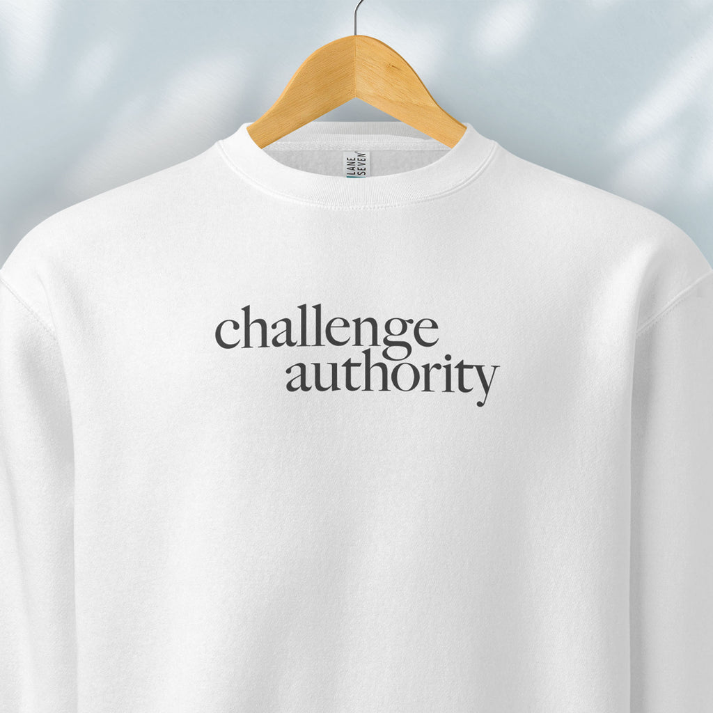 Hanging white sweatshirt with minimalist serif text block reading “challenge authority."