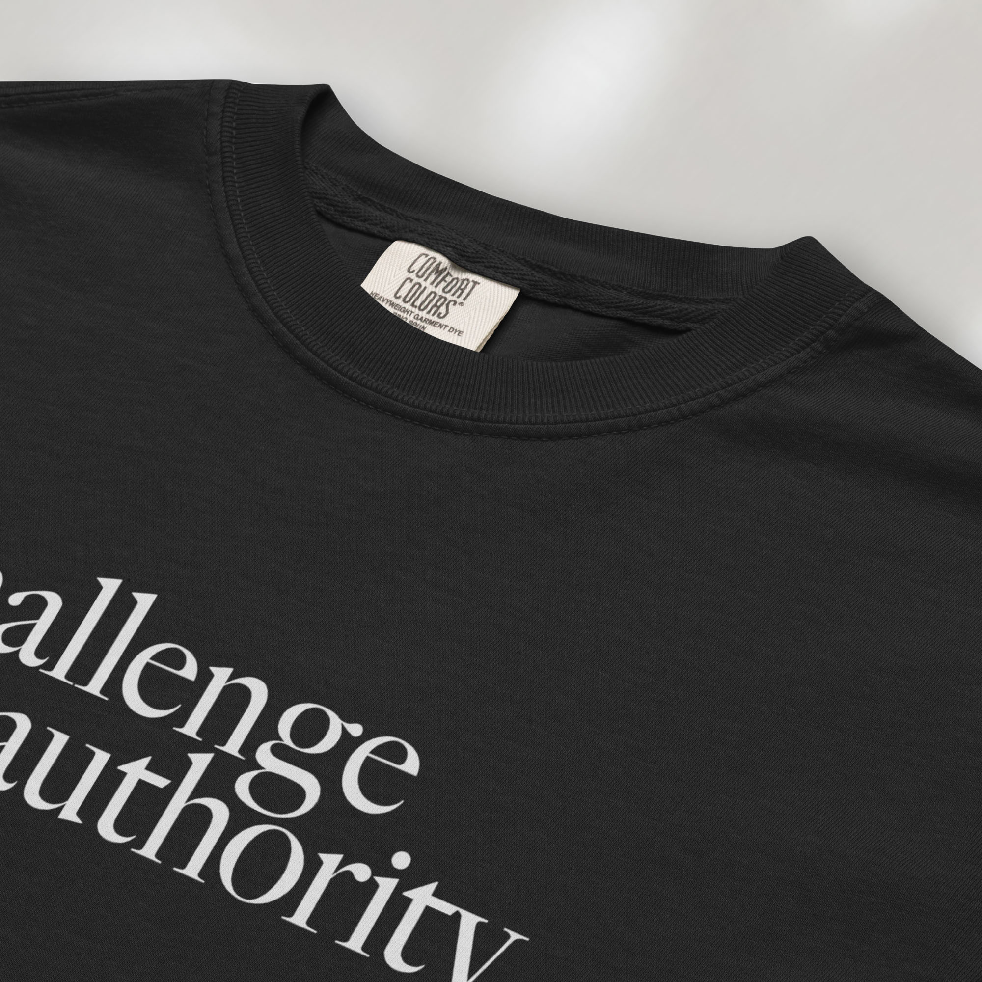 Closeup detail of black t-shirt with minimalist serif text block reading “challenge authority."