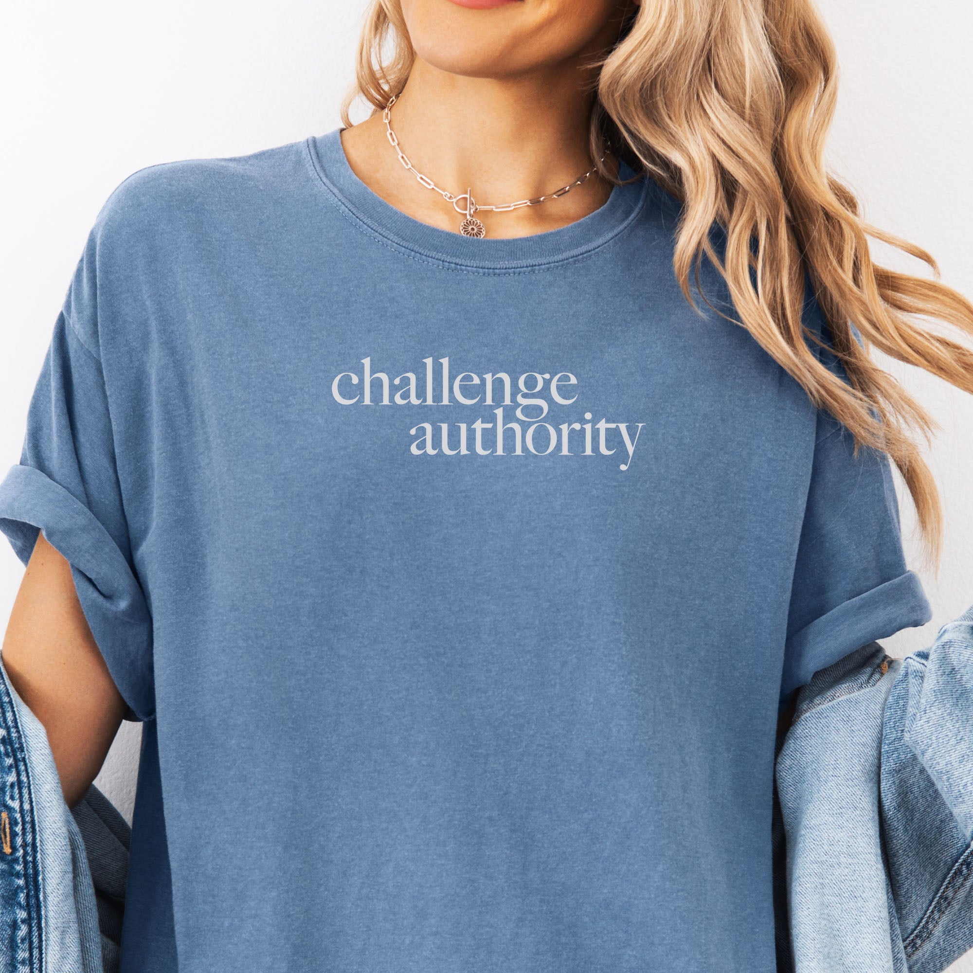 Female model wearing oversized blue jean t-shirt with minimalist serif text block reading “challenge authority."