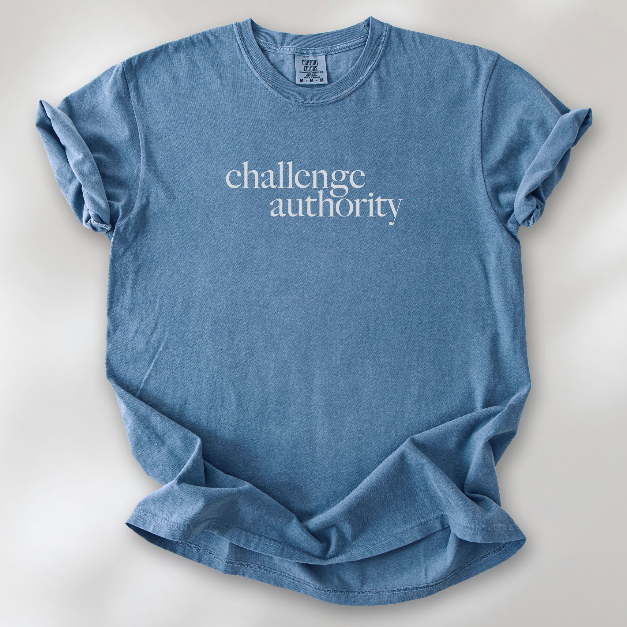 Blue jean t-shirt with minimalist serif text block reading “challenge authority."