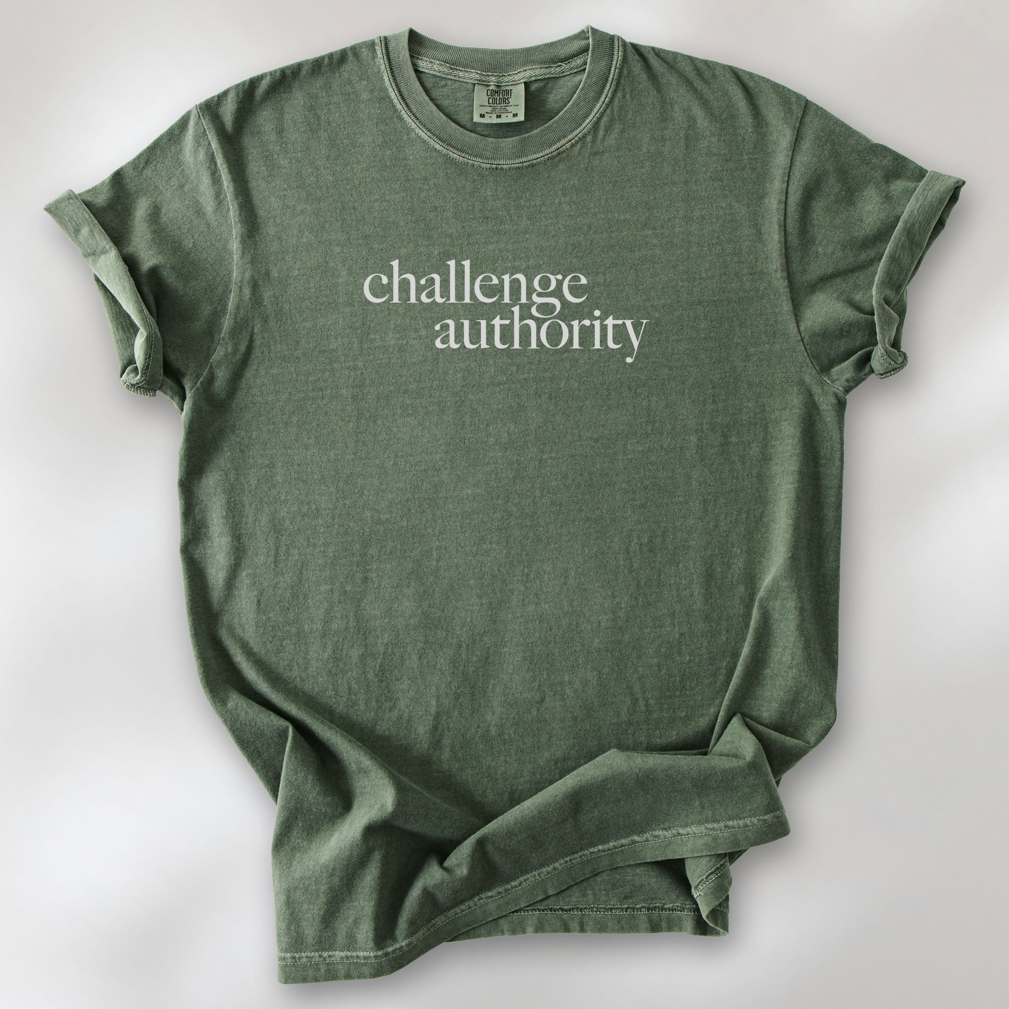 Moss t-shirt with minimalist serif text block reading “challenge authority."