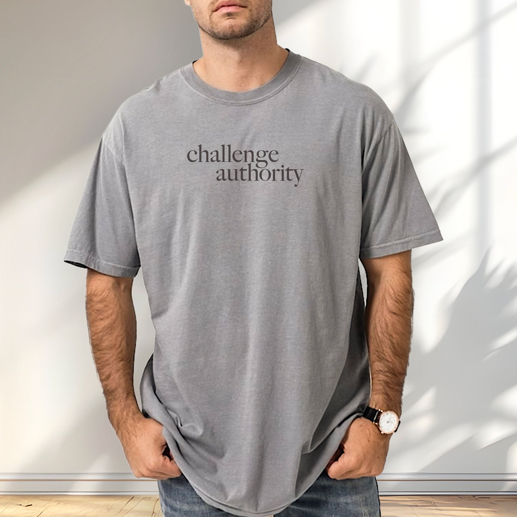 Male model wearing grey t-shirt with minimalist serif text block reading “challenge authority."