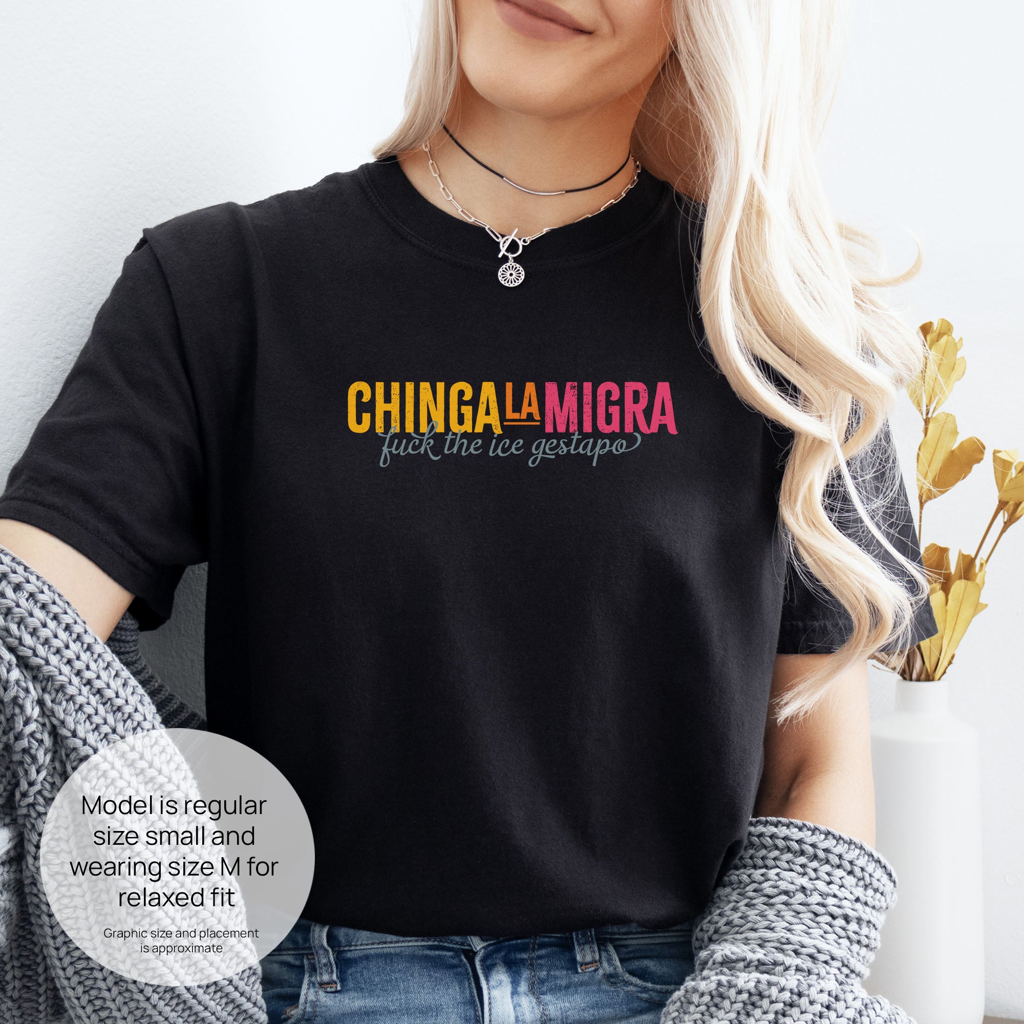 Female mode wearing black t-shirt with brightly colored text that reads "chinga la migra", with subtle script text below that says "fuck the ice gestapo." Includes size and fit information for the model who is regular size small, and wearing a size M shirt for a relaxed fit.
