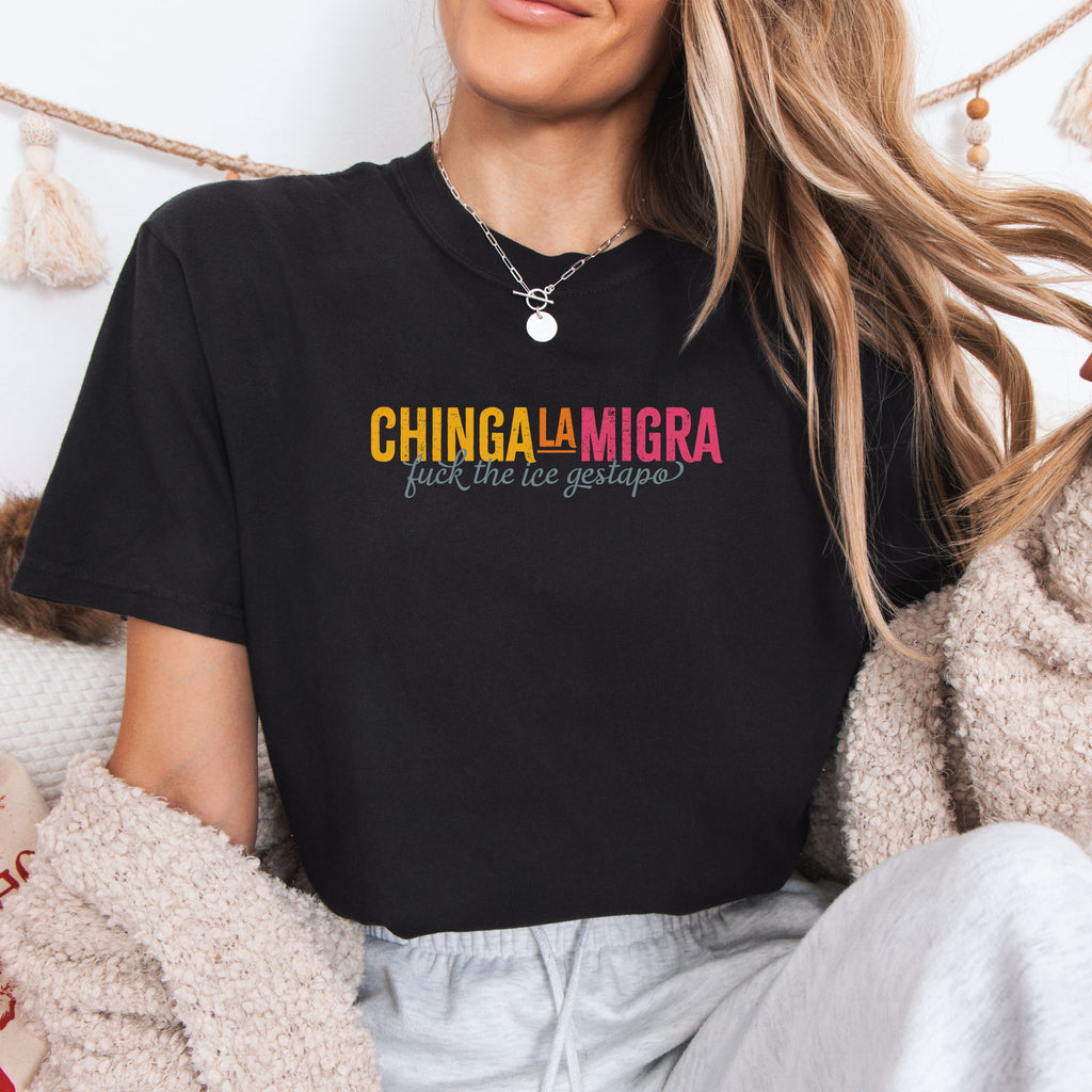 Female model wearing black t-shirt with brightly colored text that reads "chinga la migra", with subtle script text below that says "fuck the ice gestapo."