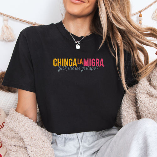 Female model wearing black t-shirt with brightly colored text that reads "chinga la migra", with subtle script text below that says "fuck the ice gestapo."