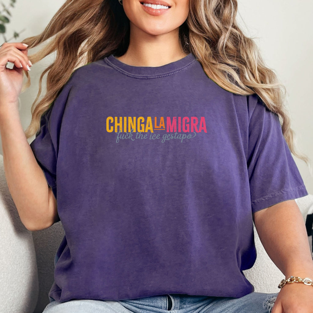 Female model wearing grape t-shirt with brightly colored text that reads "chinga la migra", with subtle script text below that says "fuck the ice gestapo."
