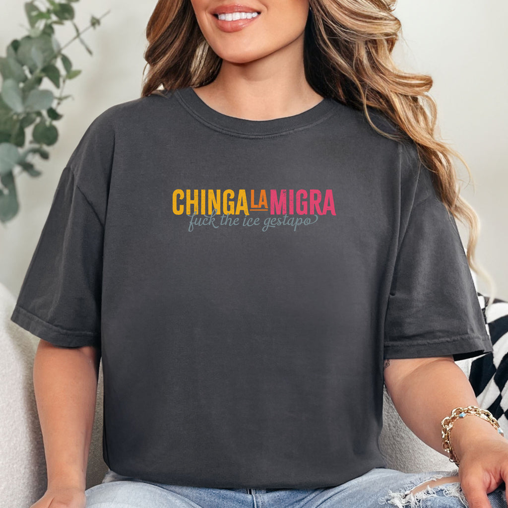 Female model wearing graphite t-shirt with brightly colored text that reads "chinga la migra", with subtle script text below that says "fuck the ice gestapo."